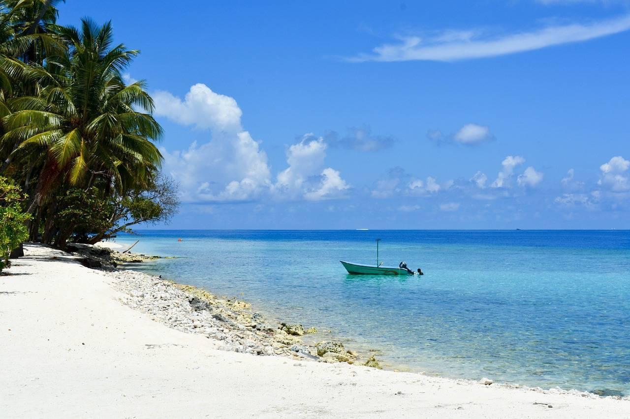 Una spiaggia di sabbia bianca con palme, barca da pesca turchese e acqua cristallina sotto un cielo tropicale blu