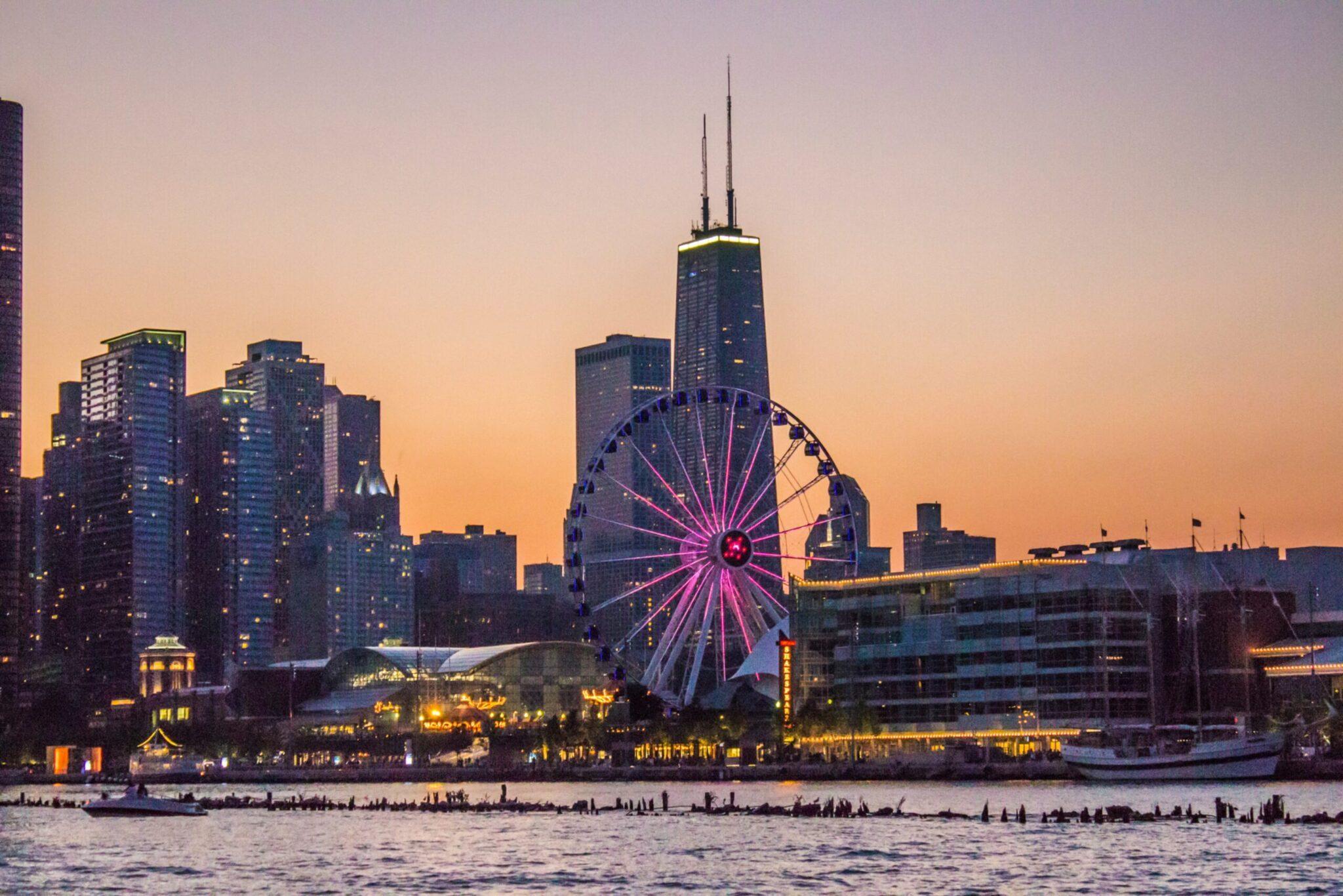 Stadtsilhouette bei Sonnenuntergang mit einem rosa beleuchteten Riesenrad und Wolkenkratzern am Wasser