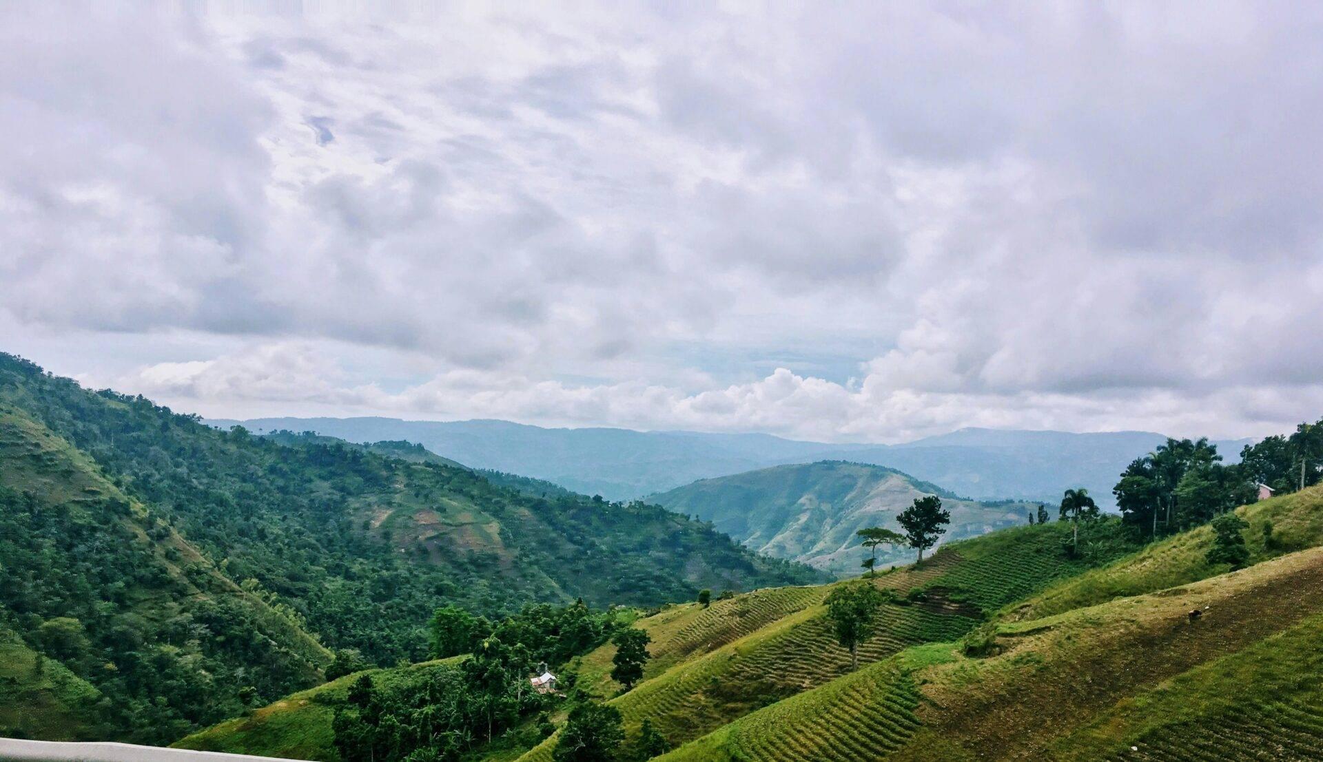 Valles verdes y colinas cultivadas con casas dispersas bajo un cielo nublado en una región montañosa tropical