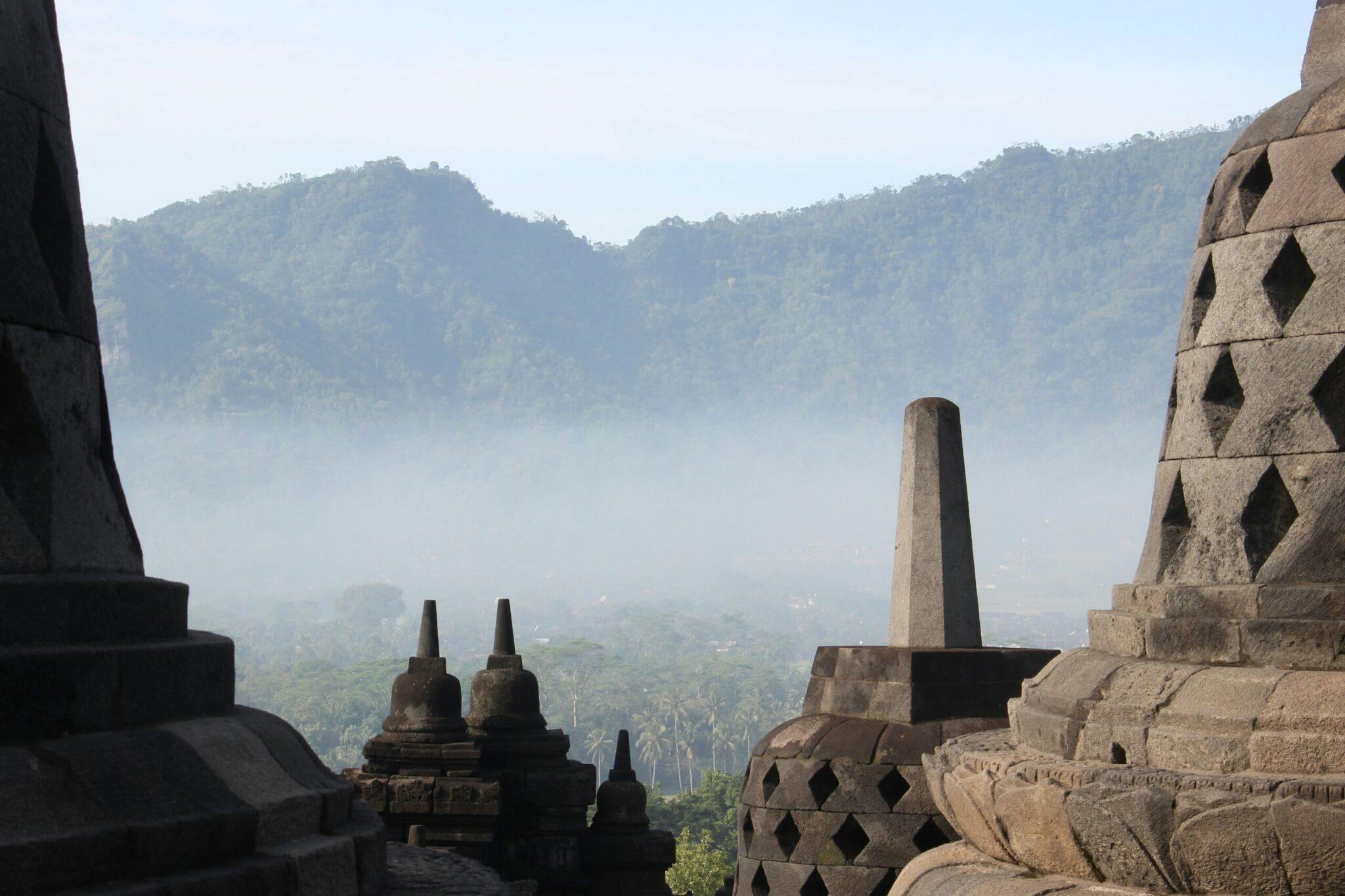 Blick von einem buddhistischen Tempel auf ein von dichtem Tropenwald bedecktes Bergtal im Morgendunst