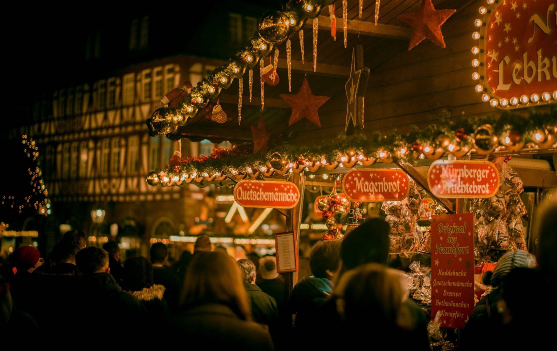 Un mercado navideño alemán iluminado de noche con casetas decoradas, estrellas doradas y visitantes paseando