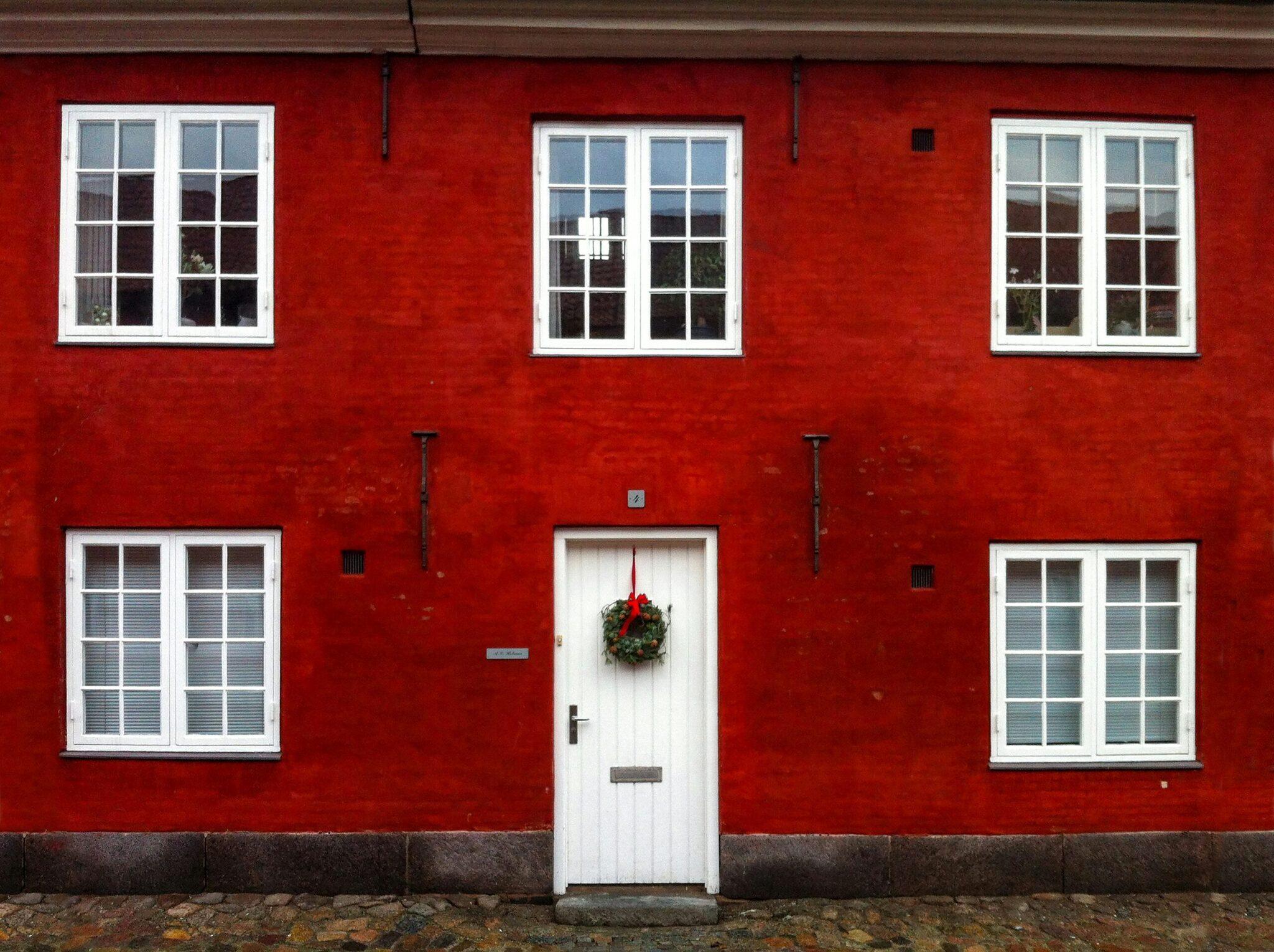Fachada roja de una casa escandinava tradicional con puerta blanca decorada con una corona navideña