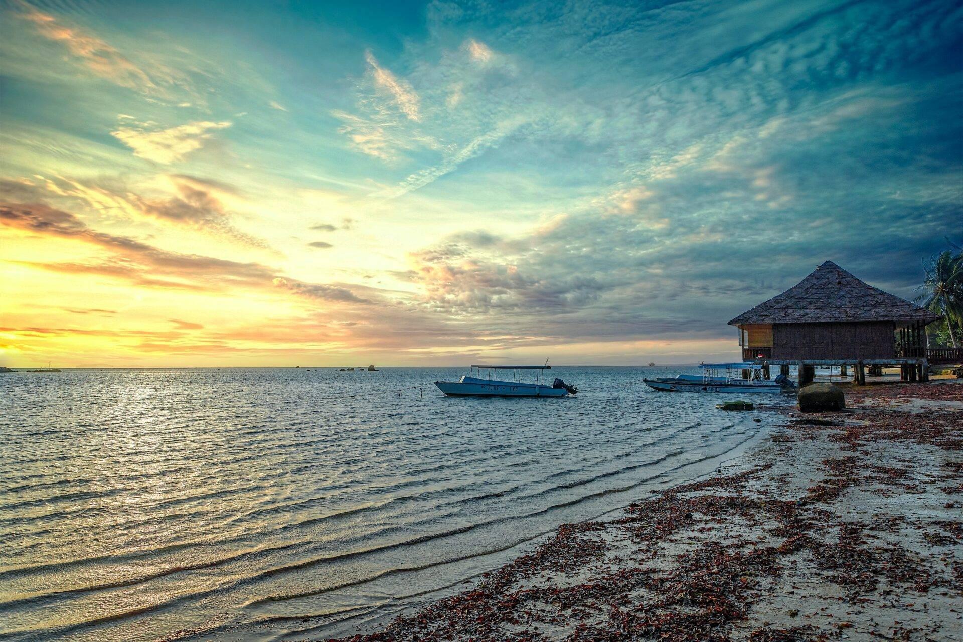 Tramonto tropicale su una spiaggia di sabbia con bungalow su palafitte e barche da pesca all’ancora