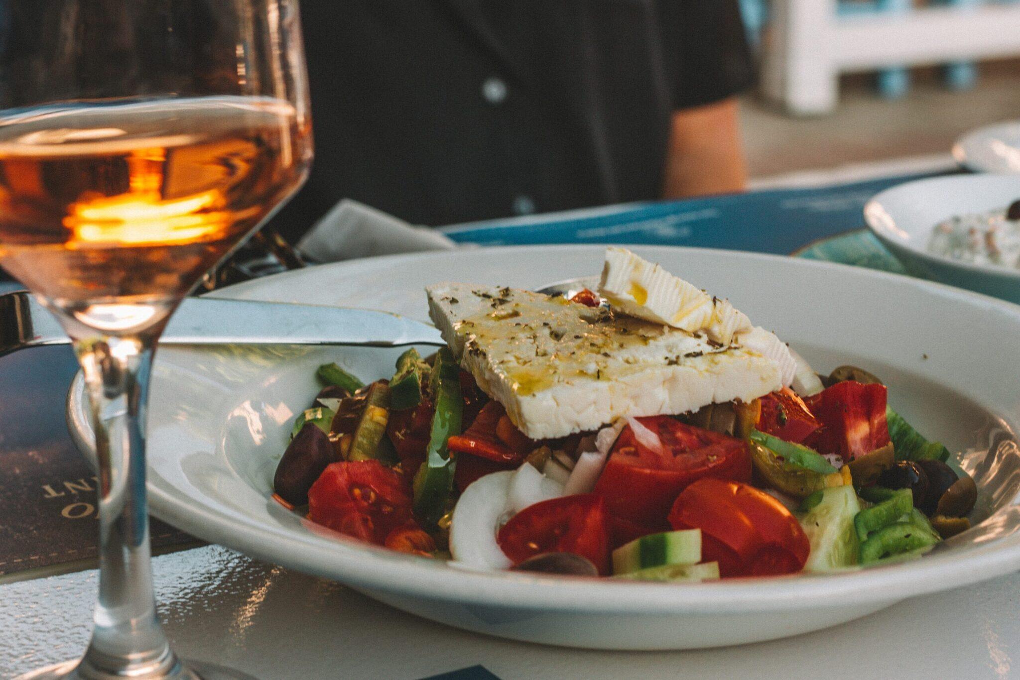 Piatto di insalata mediterranea con feta e bicchiere di vino rosato su una terrazza soleggiata