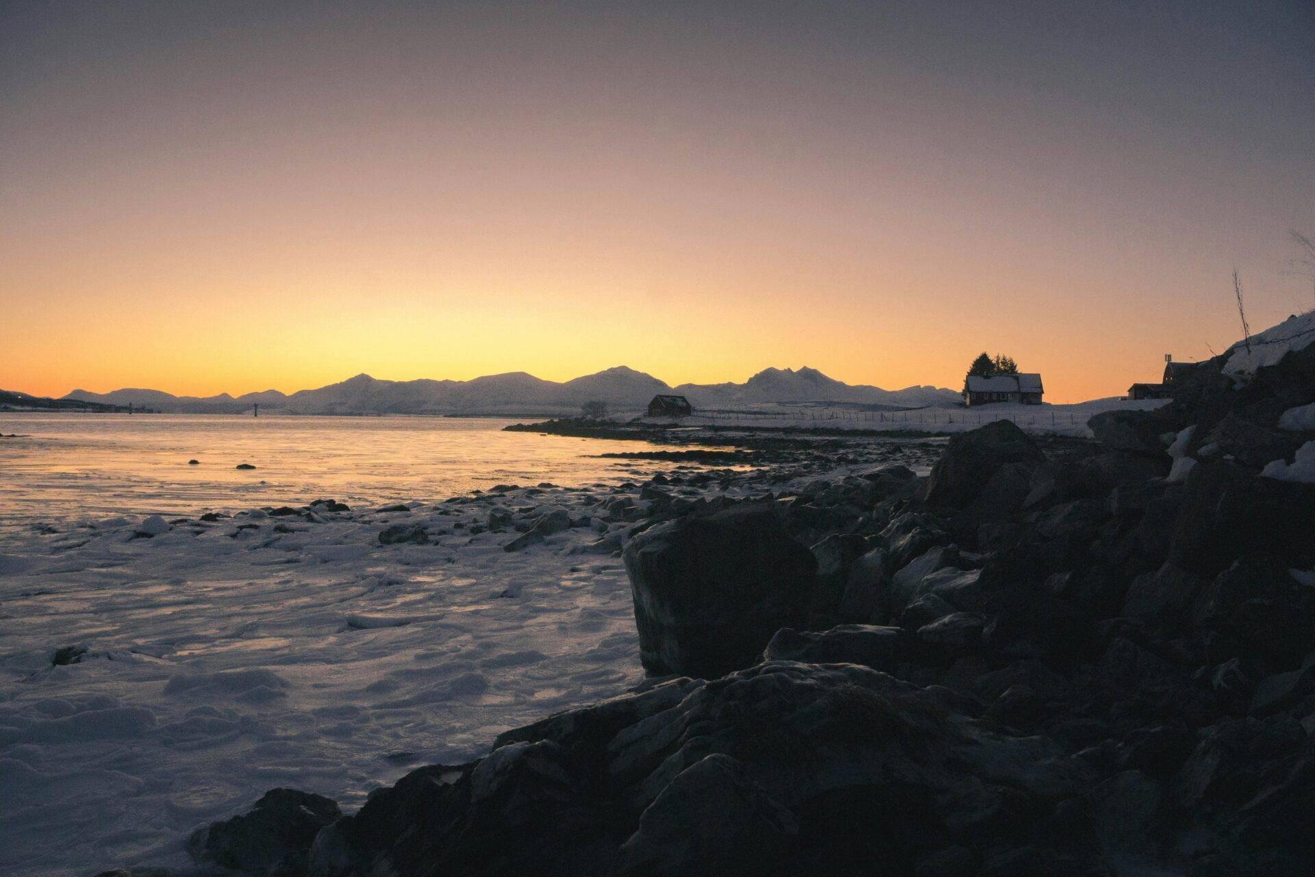 Sonnenuntergang über einer Felsenküste mit Küstengebäuden und Bergen im Hintergrund