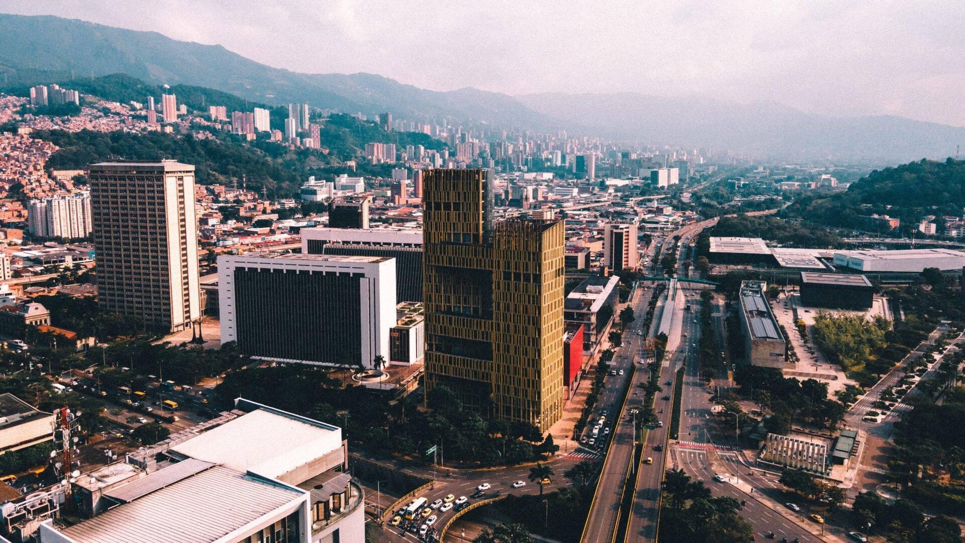Vista aérea de una metrópoli colombiana con rascacielos modernos, montañas verdes y densa urbanización en torno al centro