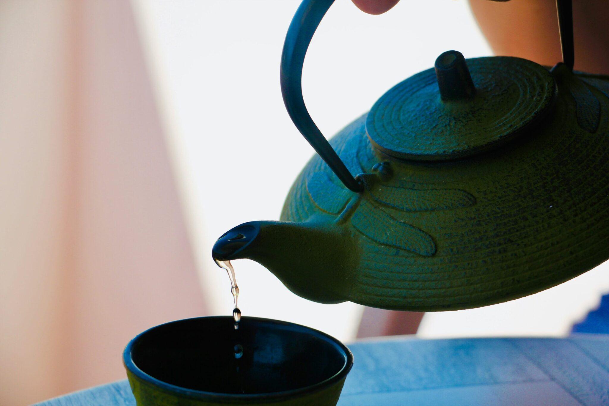 Eine blaue gusseiserne Teekanne gießt heißen Tee in eine Tasse, Sinnbild für eine kulturelle Auszeit auf Reisen