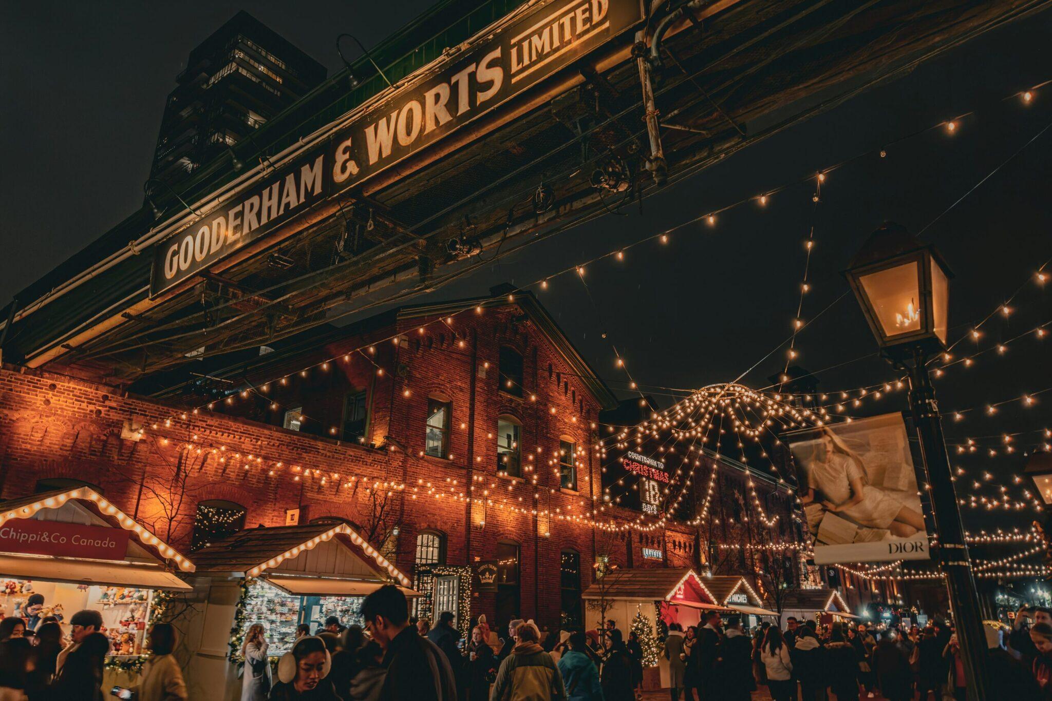 Mercatino natalizio illuminato con edifici in mattoni rossi, ghirlande luminose e folla di visitatori in serata