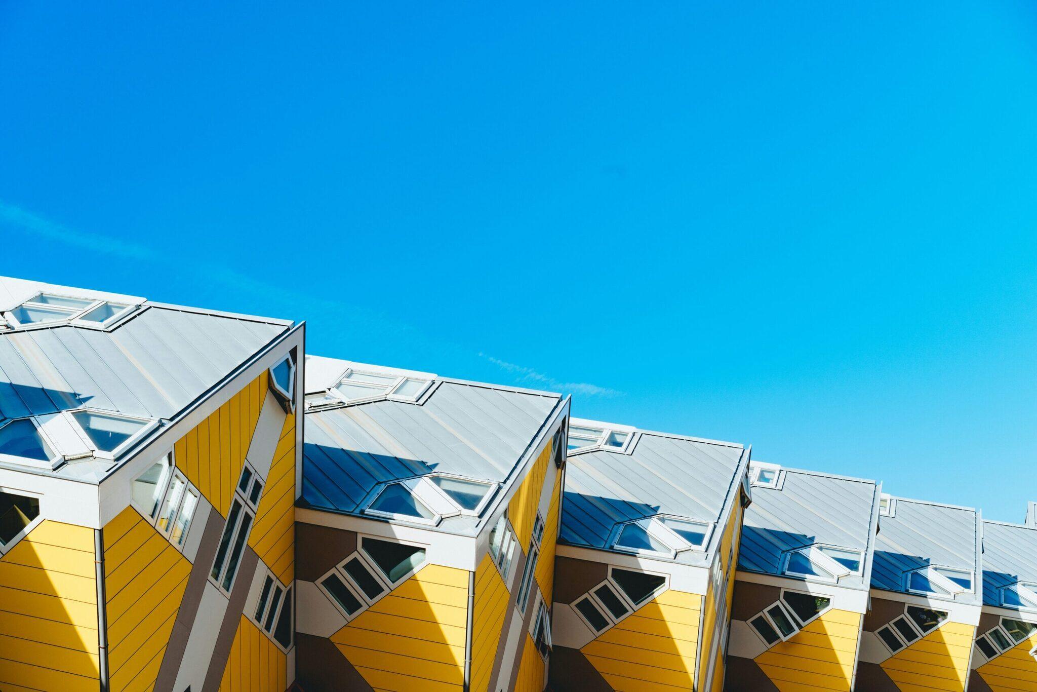 Gelbe und weiße Kubushäuser mit blauen Dächern unter klarem Himmel, markante moderne Architektur