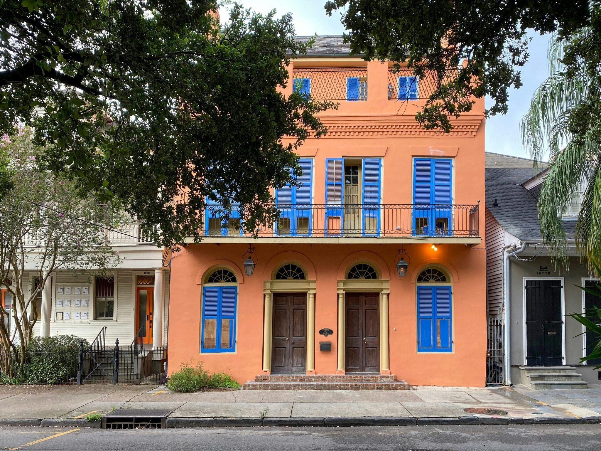 Facciata colorata arancione e blu di una casa coloniale storica fiancheggiata da alberi in una via residenziale