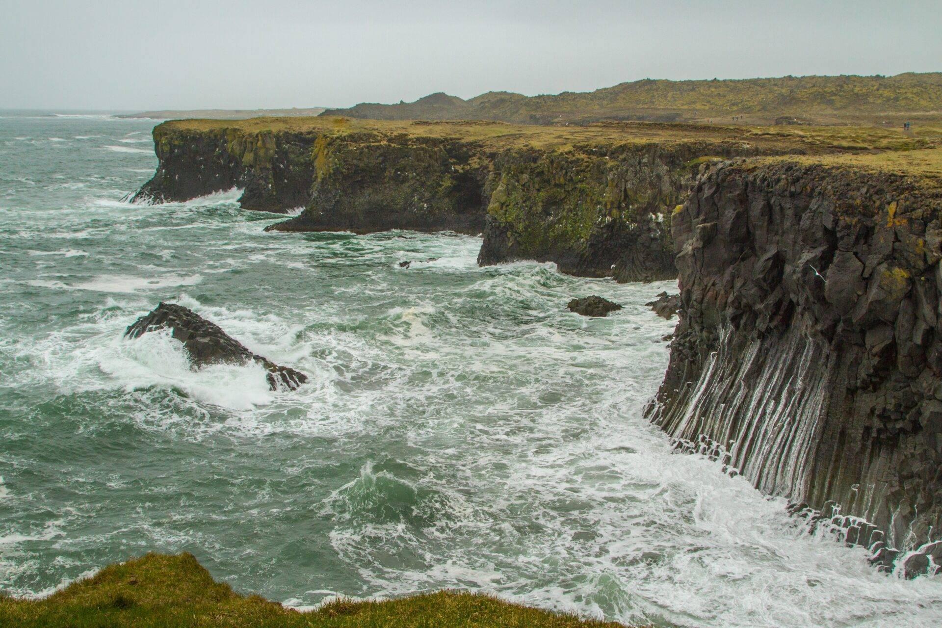Acantilados costeros de columnas basálticas con musgo verde y olas turquesas en Islandia