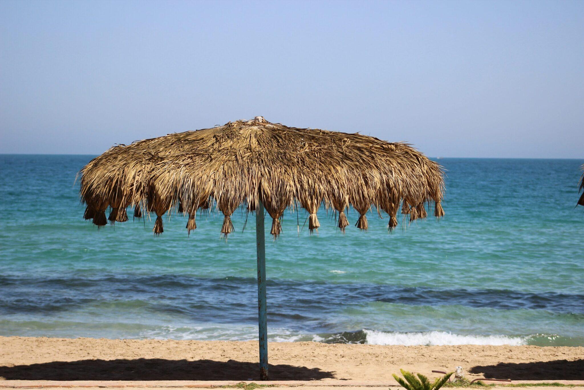 Ein geflochtener Strohhut-Sonnenschirm auf einem Sandstrand vor einem ruhigen türkisfarbenen Meer