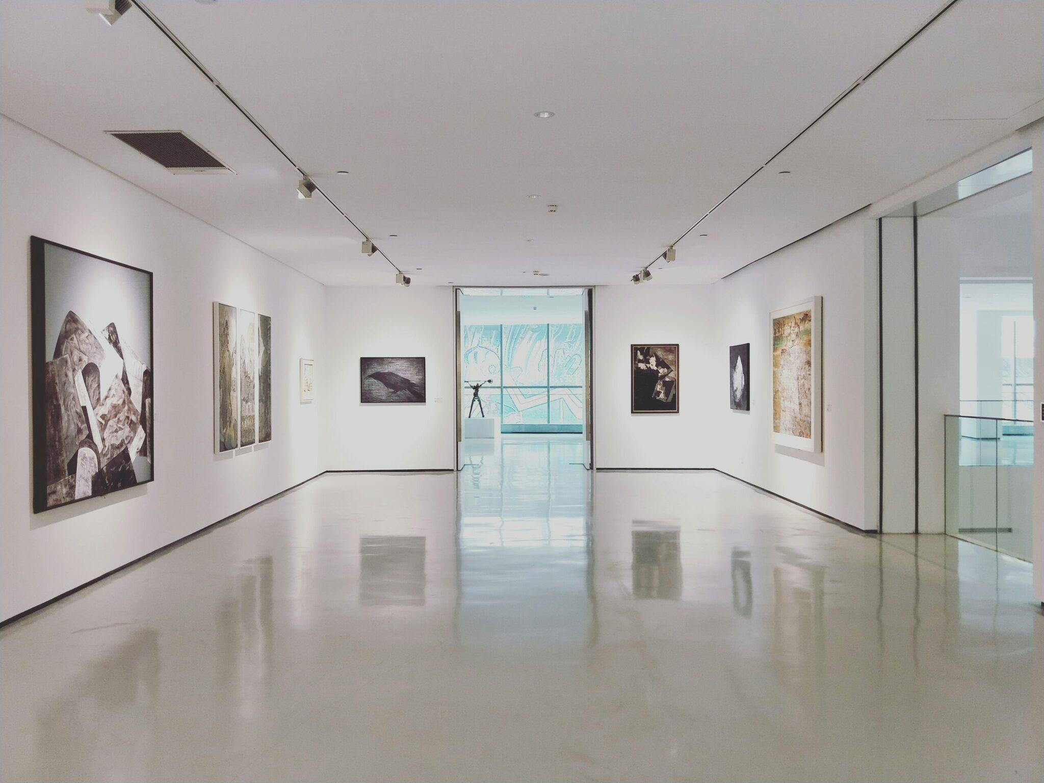 Galleria d’arte moderna con mostra fotografica, pavimento bianco lucido e ampie vetrate panoramiche sulla città