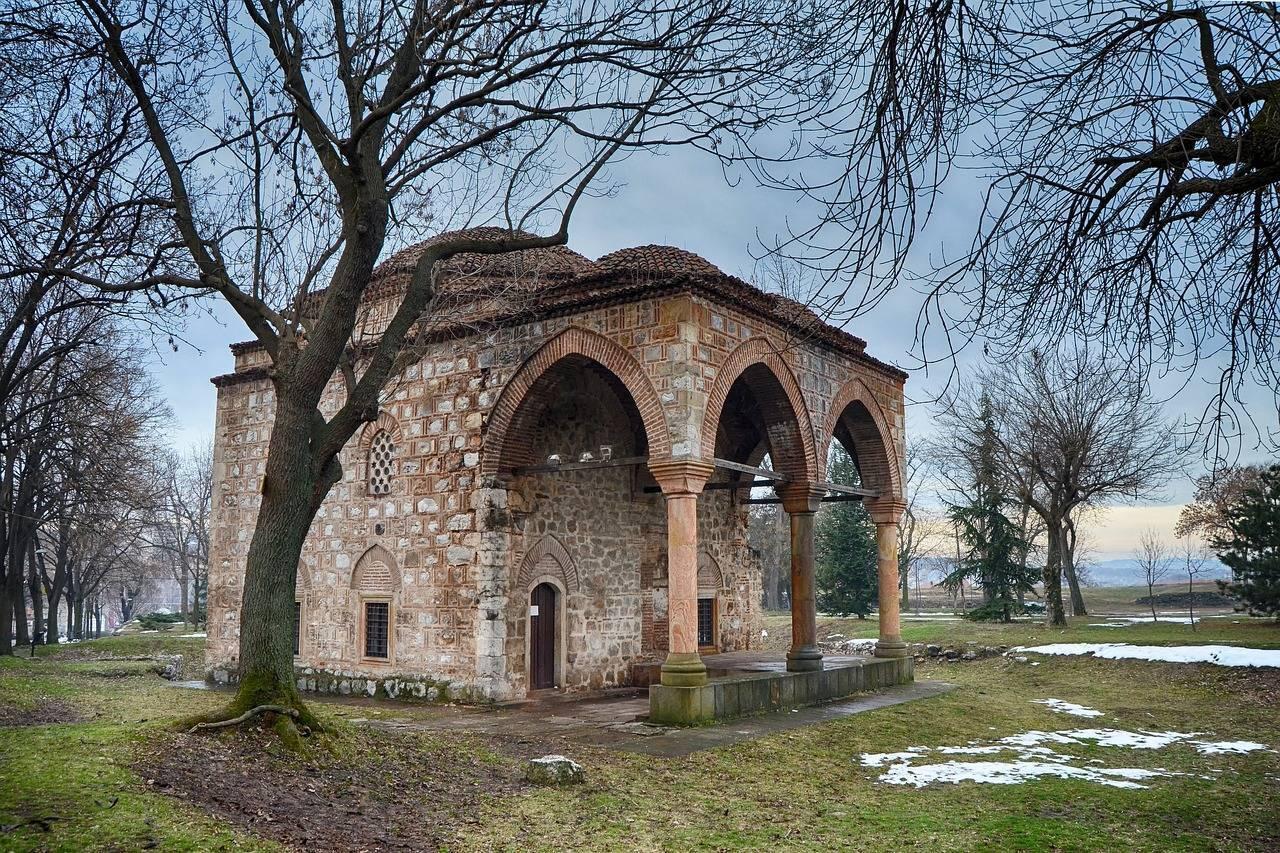 Ein historisches religiöses Gebäude aus rotem Backstein mit Arkaden, umgeben von kahlen Bäumen und Wiesen