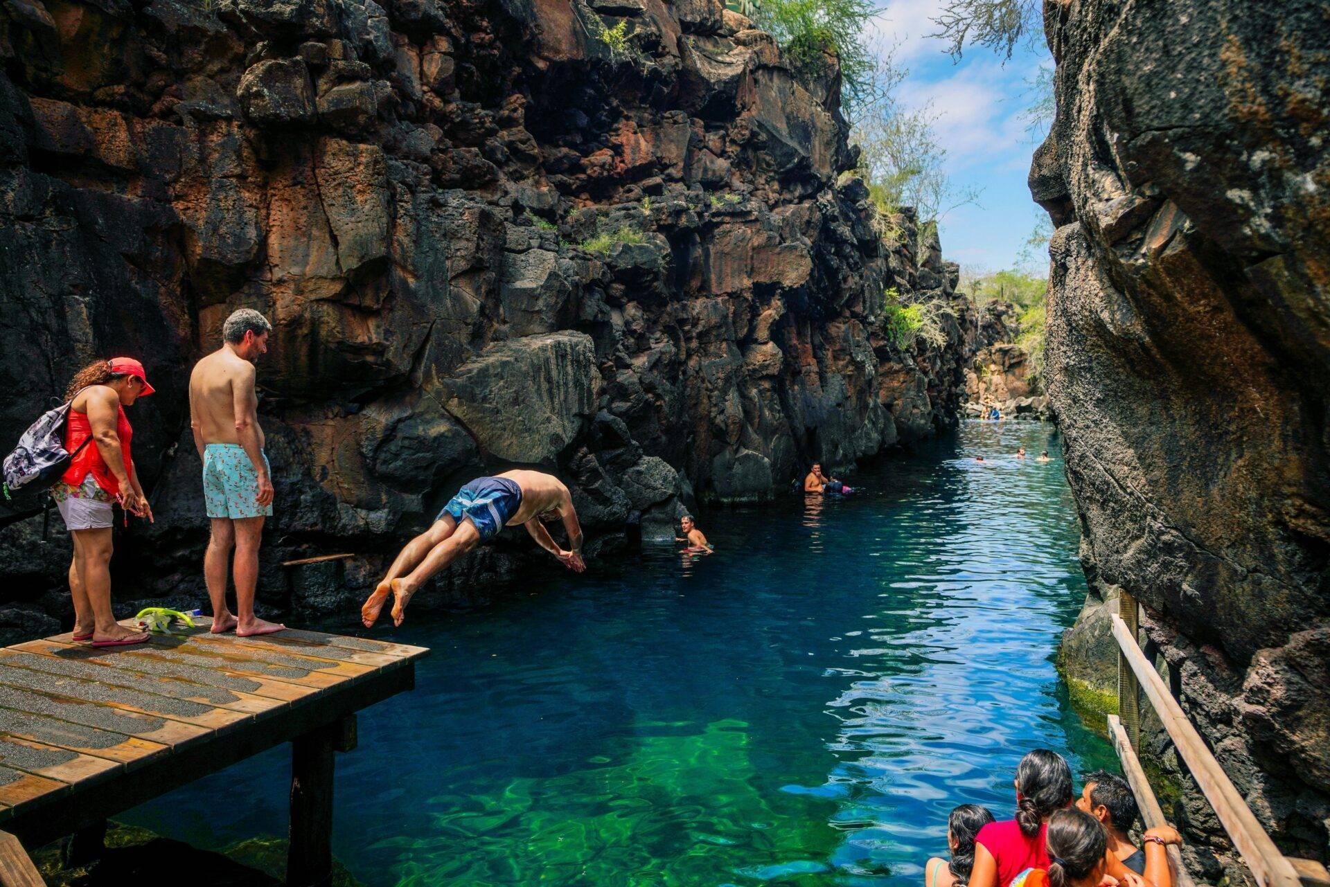 Turisti fanno snorkeling in una piscina naturale cristallina incorniciata da alte scogliere rocciose