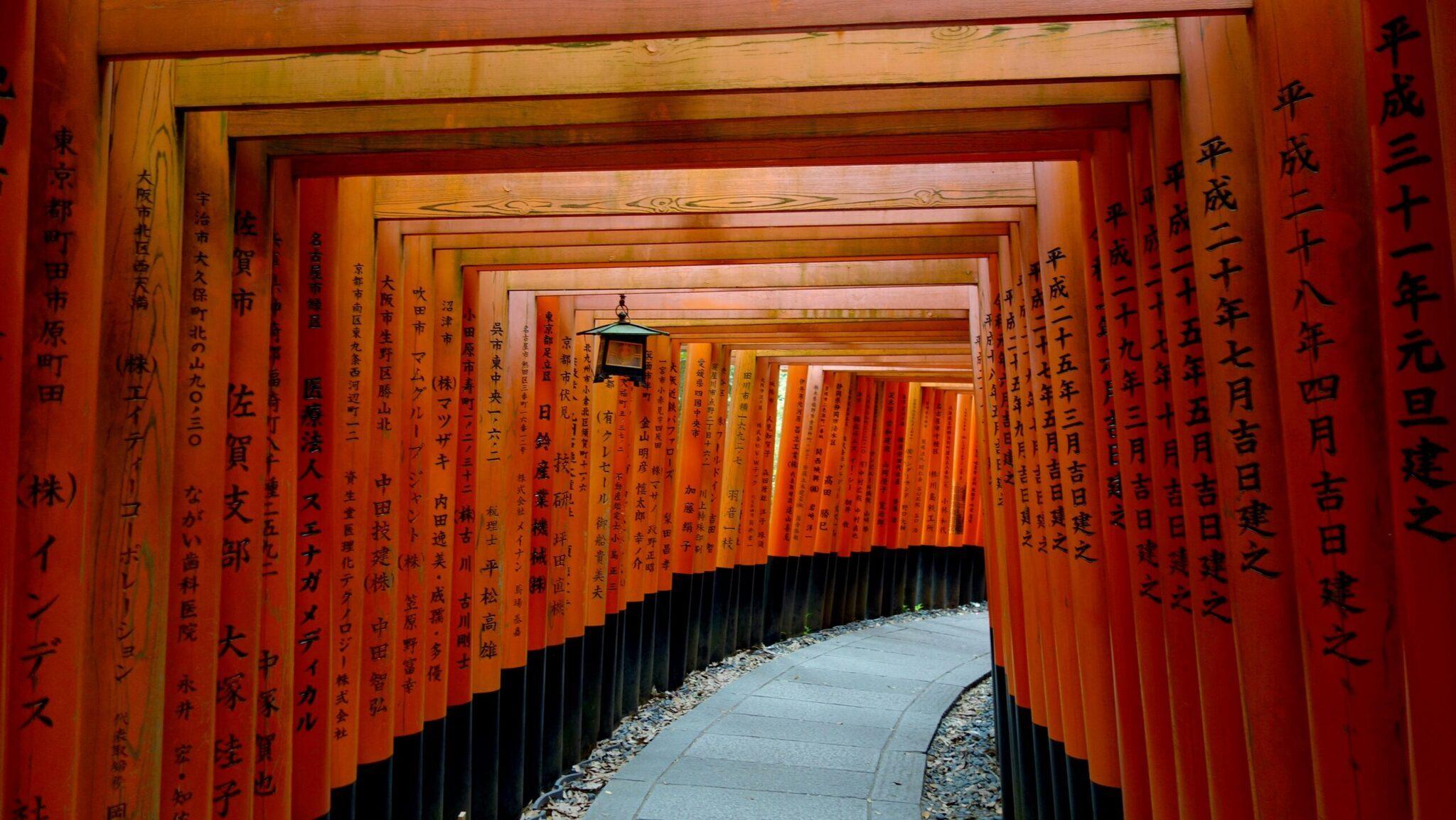 Túnel de miles de torii rojos con caracteres japoneses en un santuario tradicional