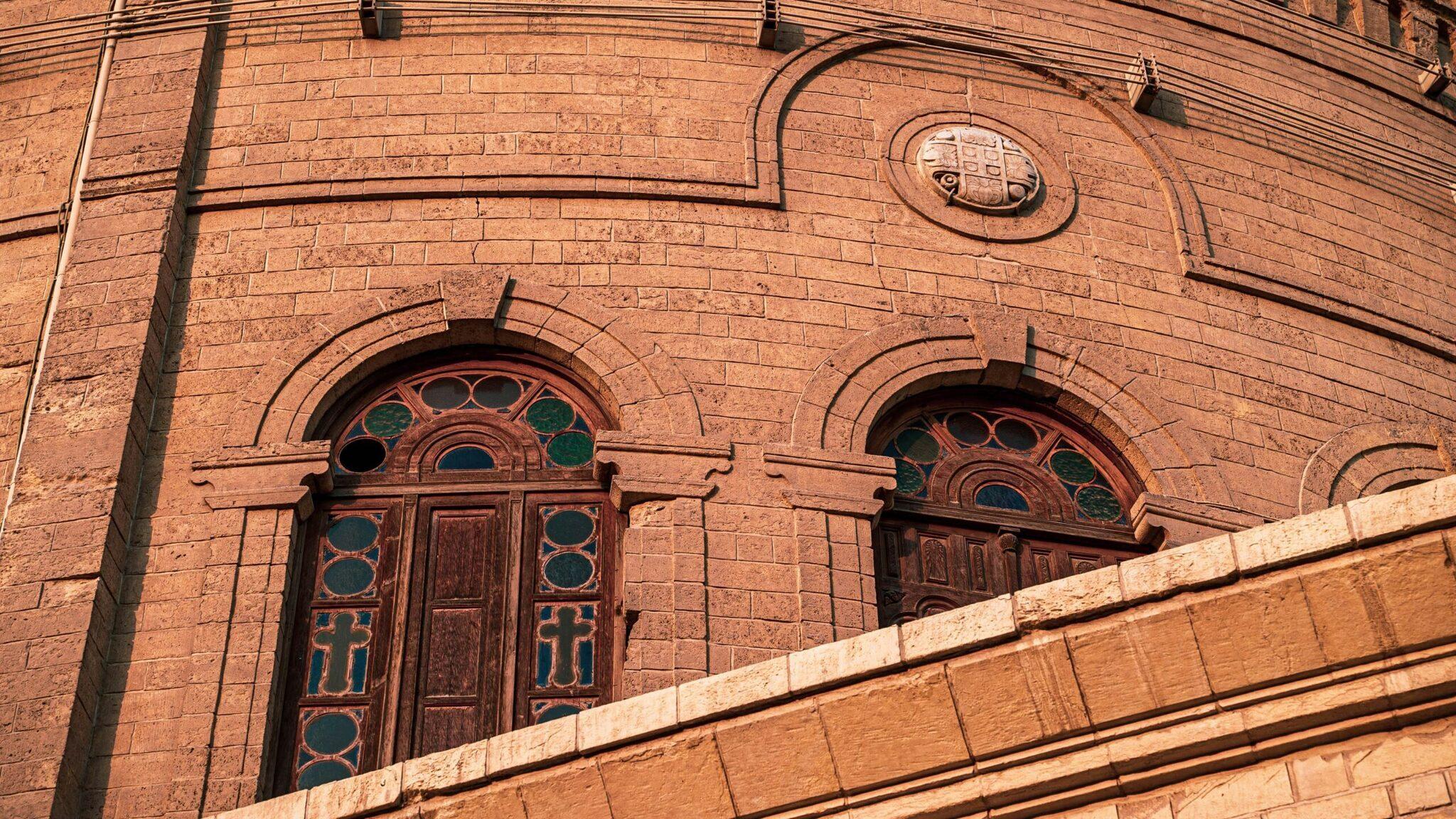 Fachada de ladrillo rojo de un edificio histórico con puertas ornamentadas de vidrieras y detalles arquitectónicos