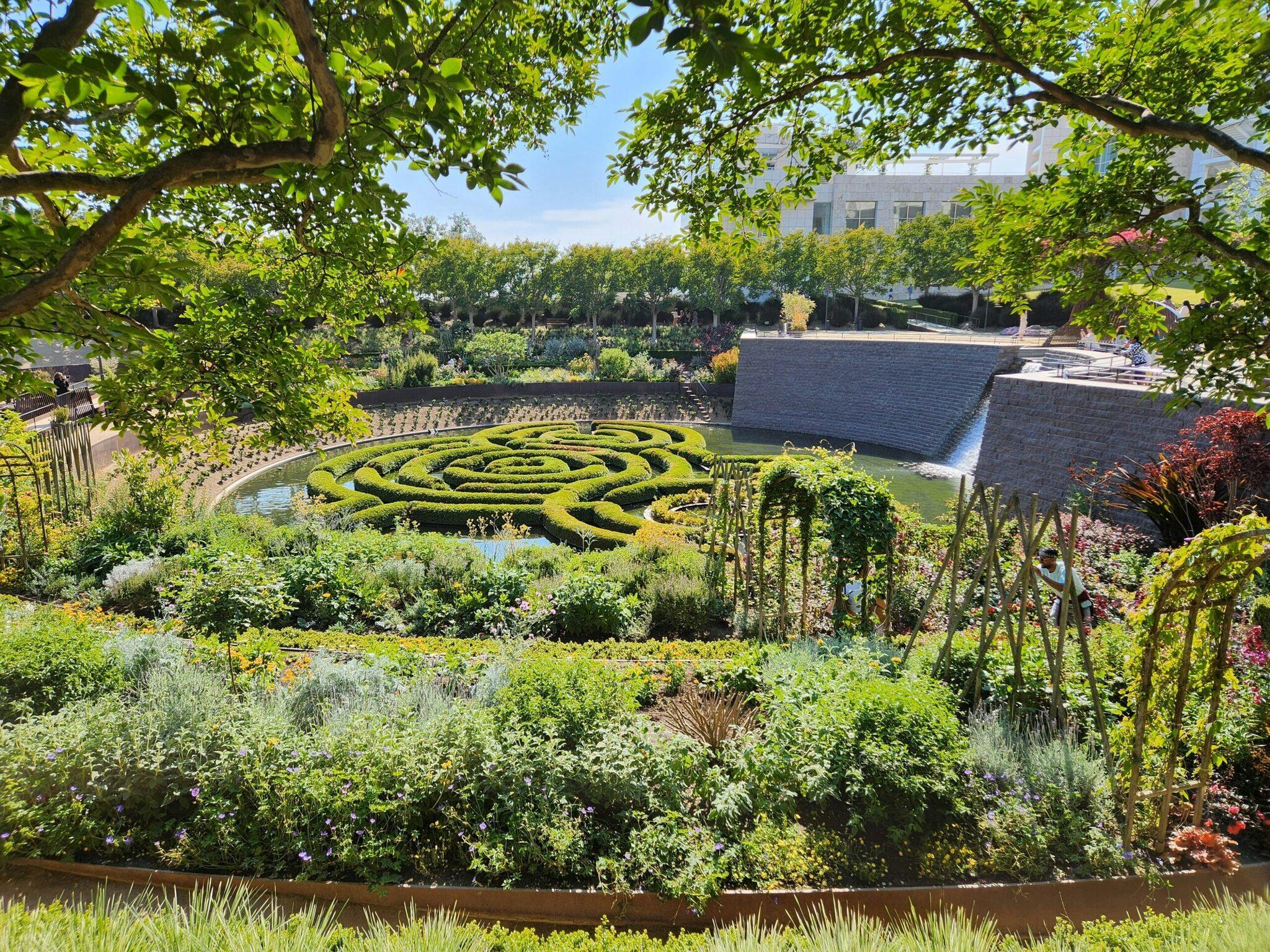 Un jardín a la francesa con un parterre de boj en espiral, estanque y edificio de piedra al fondo