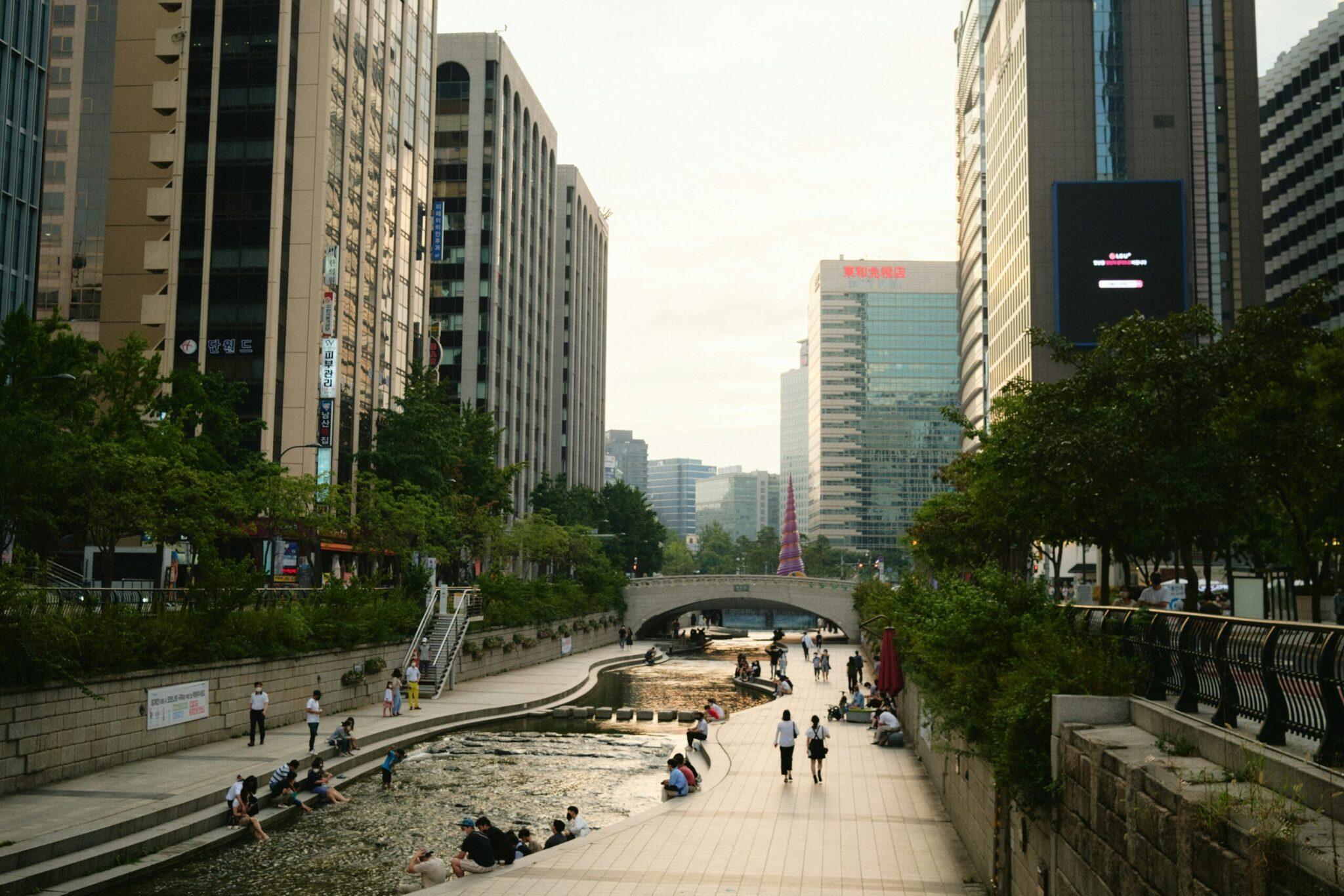 Urbaner Park mit angelegtem Bachlauf, modernen Gebäuden und Fußgängern in einer lebhaften asiatischen Metropole