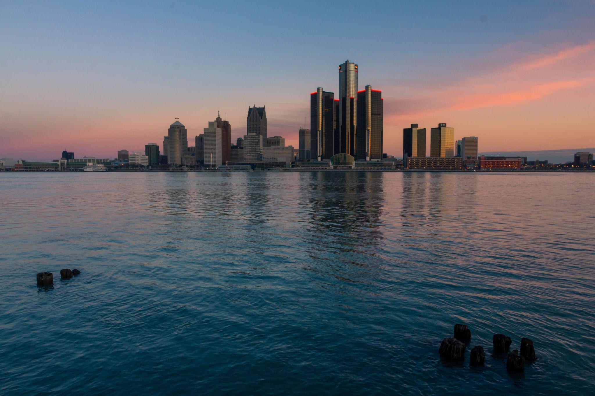 Beleuchtete Stadtsilhouette im Sonnenuntergang von einer Bucht aus, Wolkenkratzer spiegeln sich im ruhigen Wasser