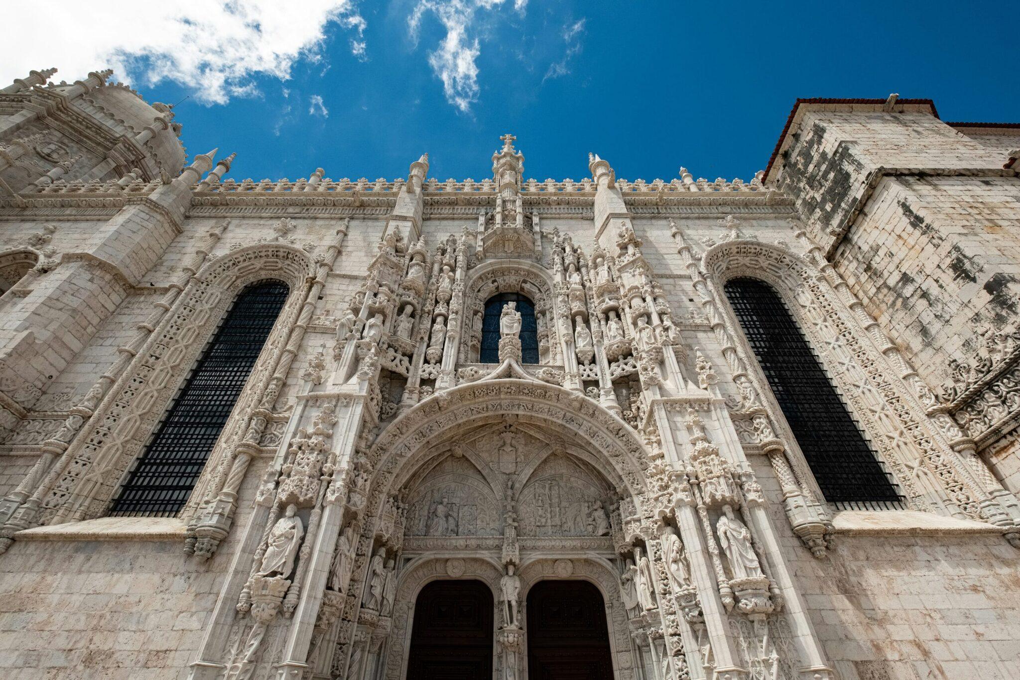 Ornamentierte Fassade einer weißen gotischen Steinkirche mit reich verziertem Hauptportal und Rosettenfenstern