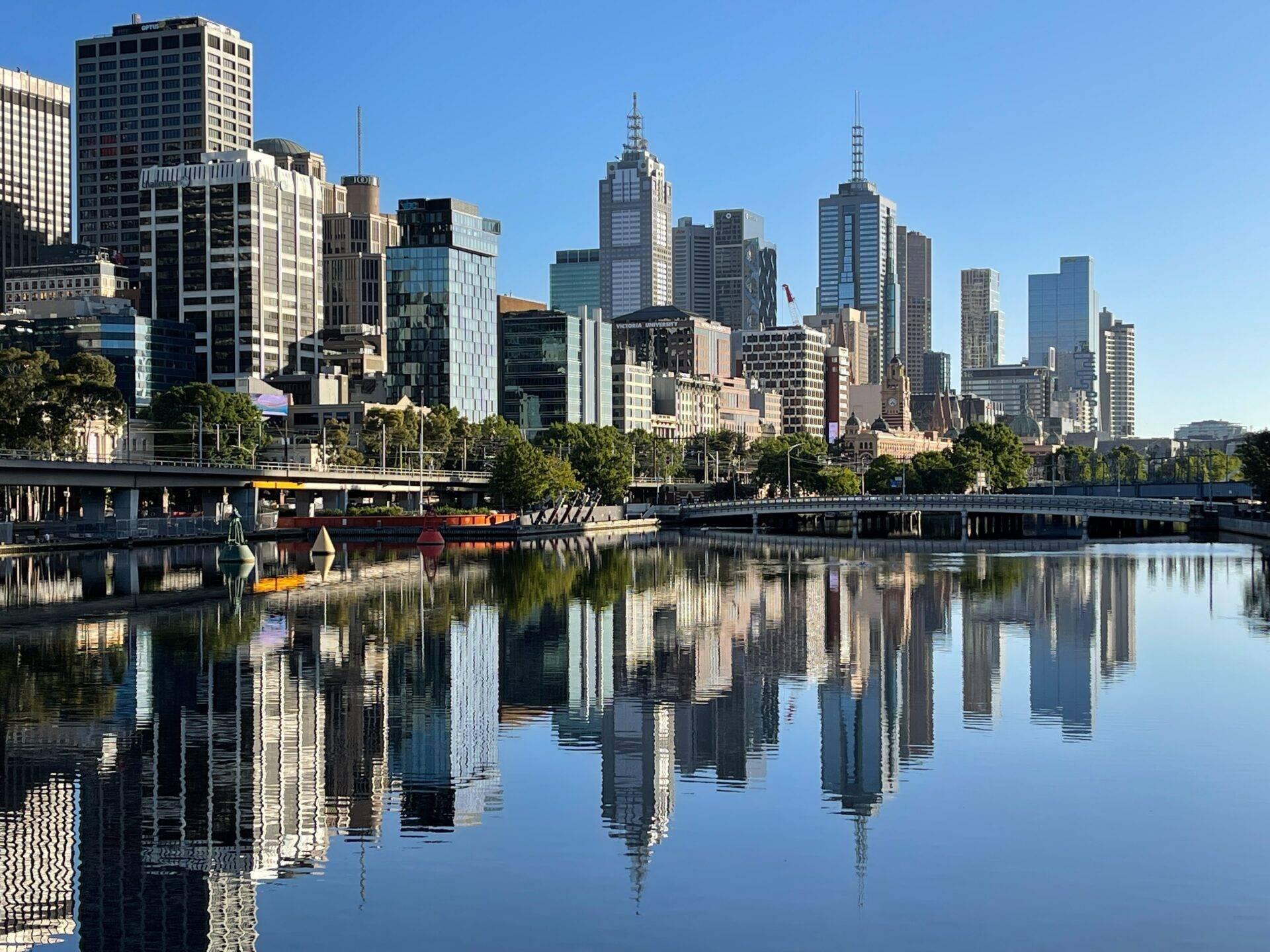 Skyline urbano moderno con grattacieli riflessi nelle acque calme di un fiume, alberi e banchine in primo piano