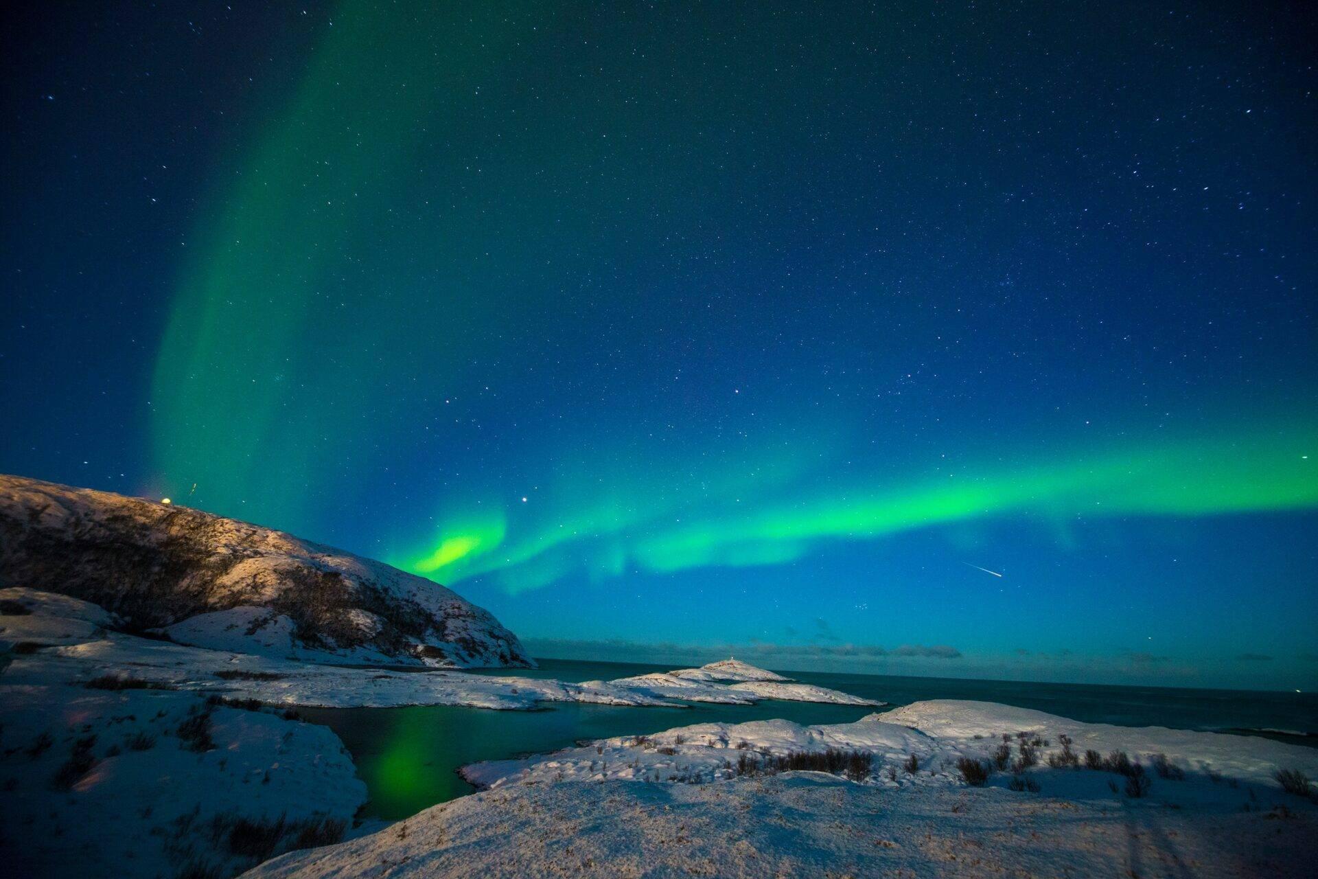 Grüne Nordlichter erhellen einen Sternenhimmel über verschneiten Bergen und zugefrorenen Seen