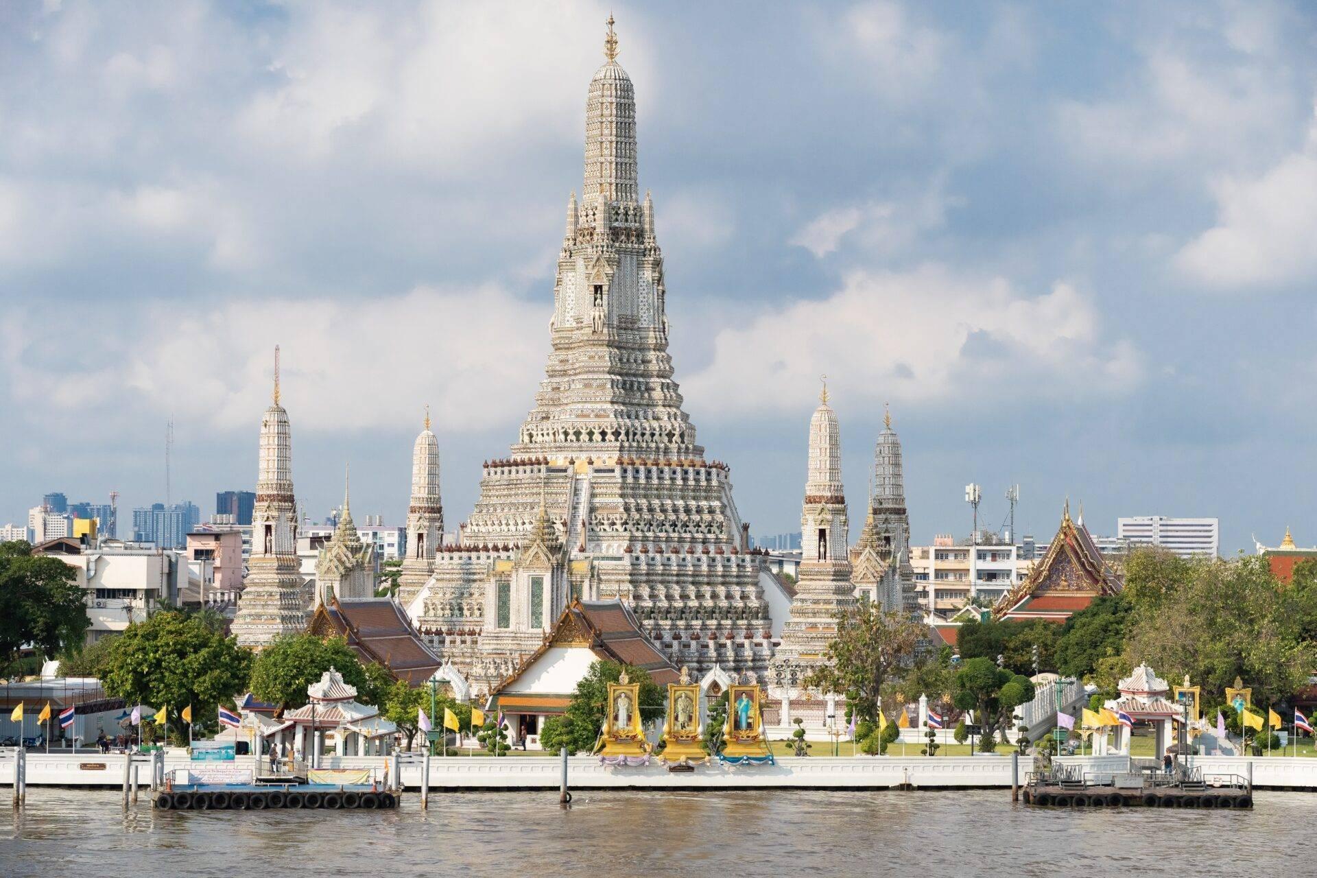 Un maestoso tempio buddista bianco e dorato con più stupa appuntiti si erge sul bordo di un fiume in Thailandia