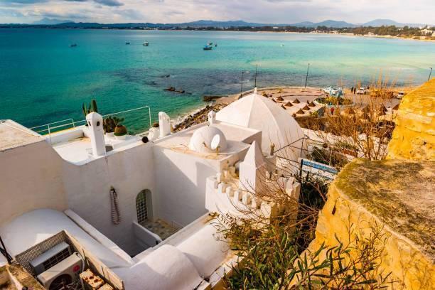 Casa blanca mediterránea encaramada en un acantilado rocoso sobre un mar turquesa con barcas