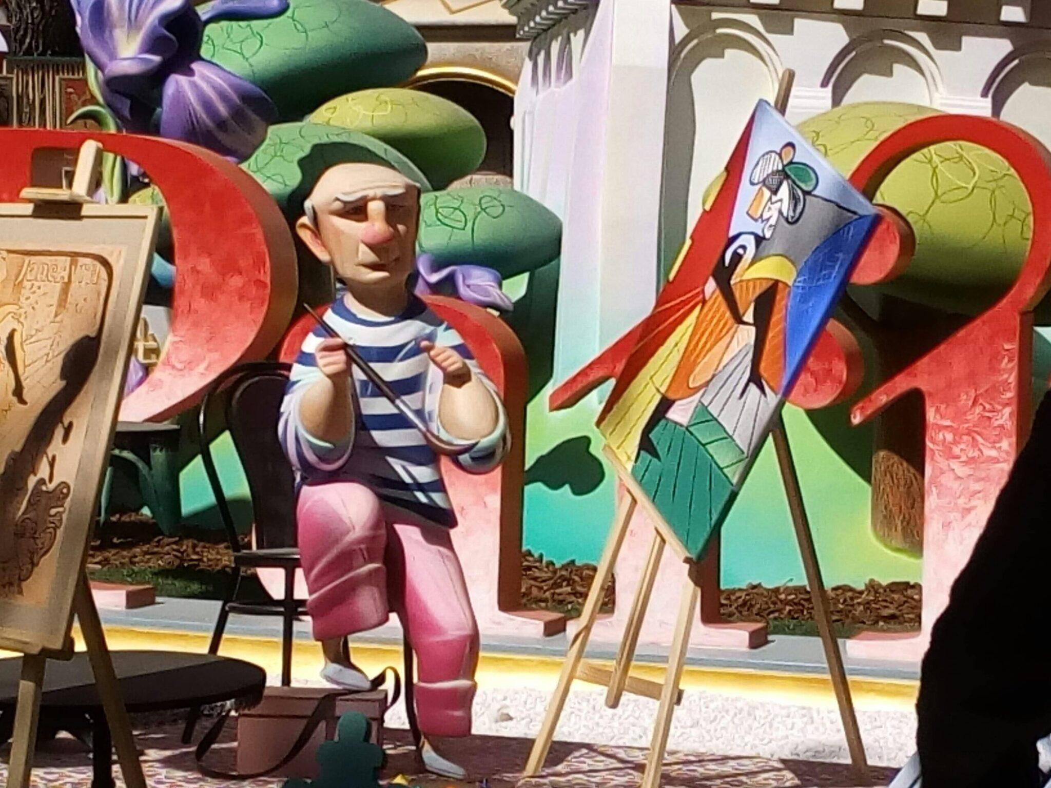 Escultura colorida que representa a un artista pintor en un decorado urbano estilizado con edificios y arquitectura