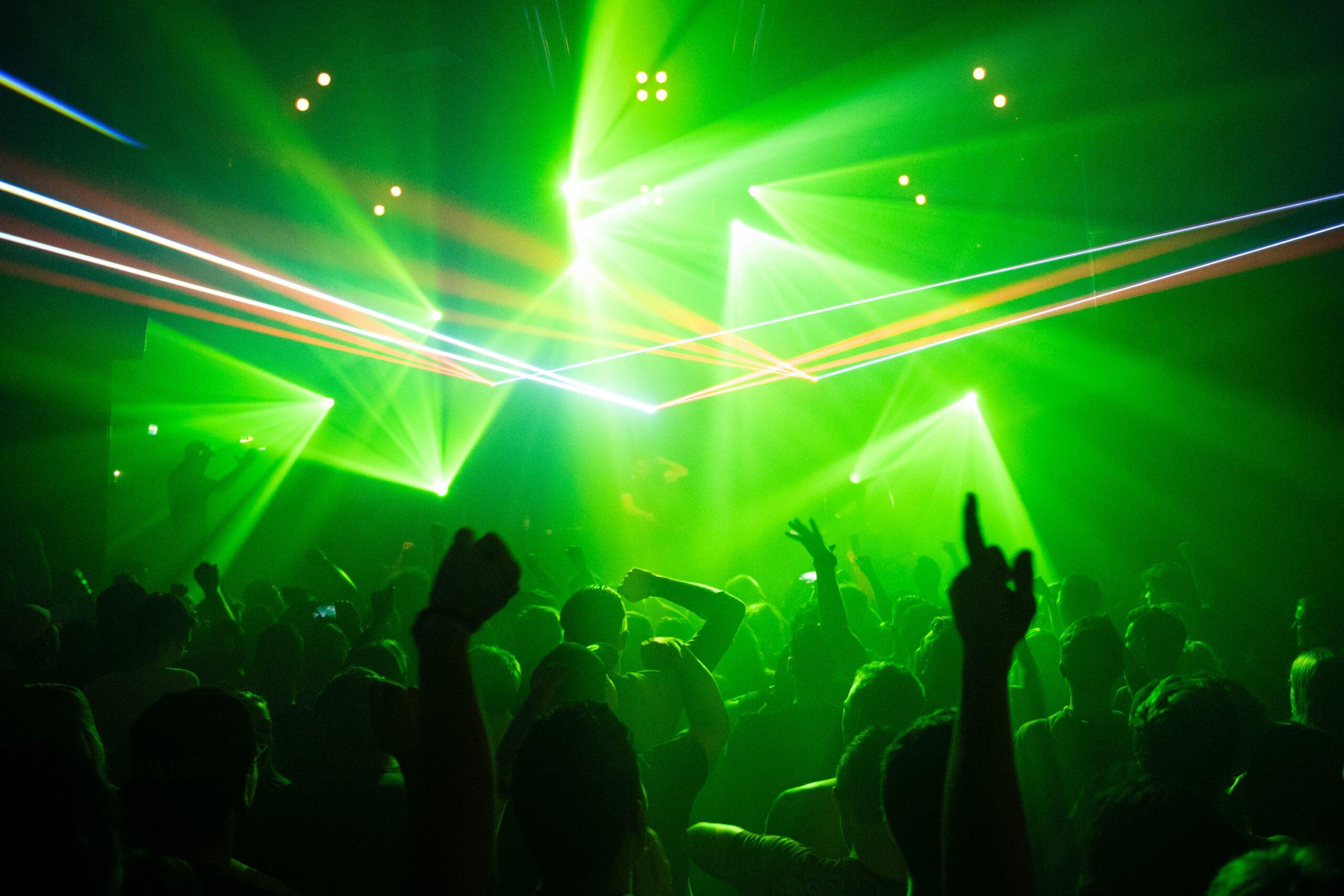 Multitud de bailarines entusiastas bajo intensos focos verdes en una discoteca