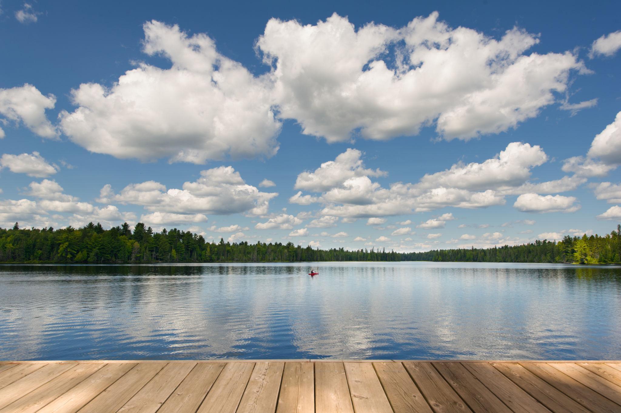 Blick von einem Holzsteg auf einen ruhigen See, umgeben von Nadelbaumwald unter bewölktem Himmel