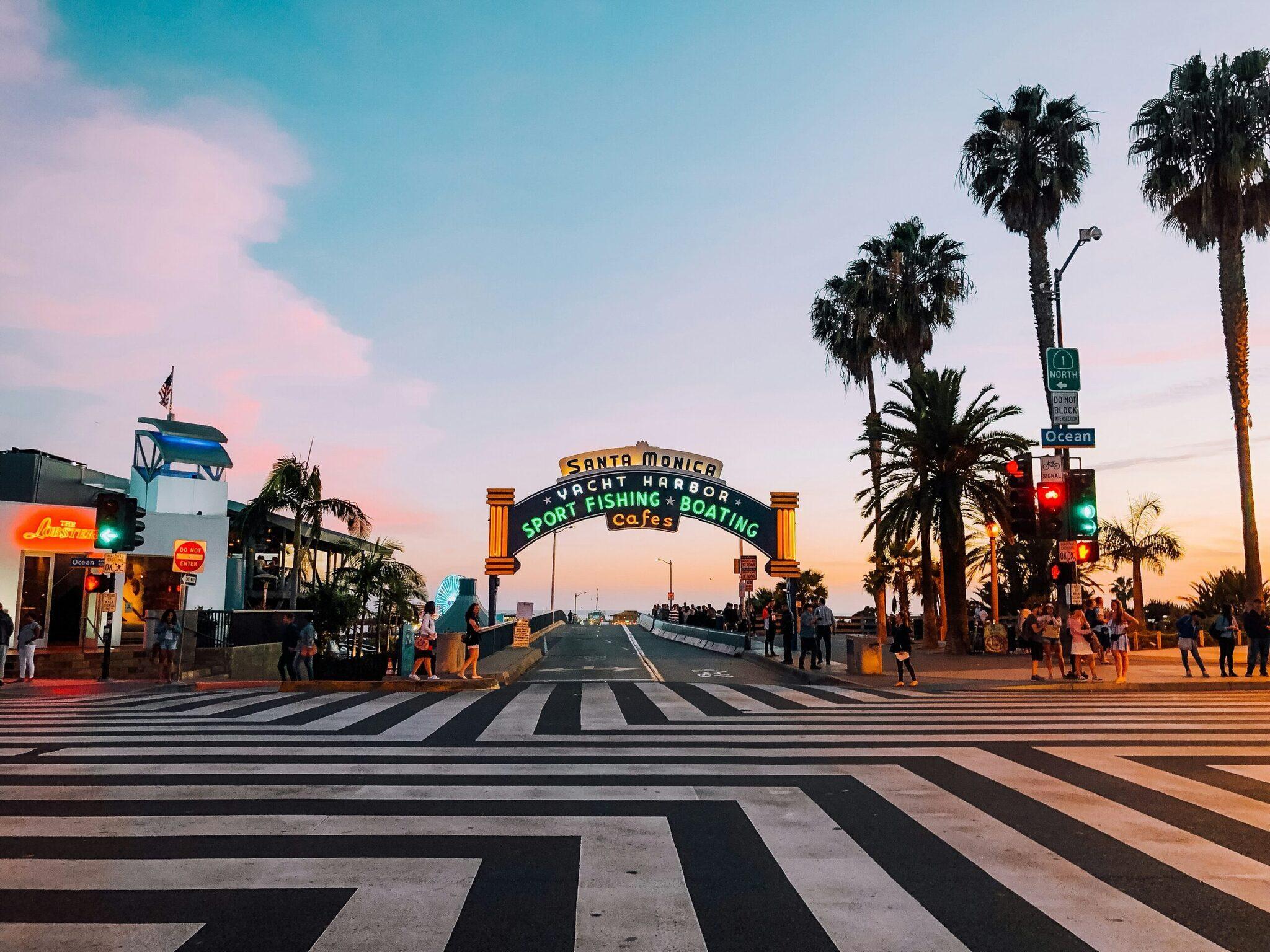 El emblemático arco del Santa Monica Yacht Harbor al atardecer, con palmeras y paseo peatonal