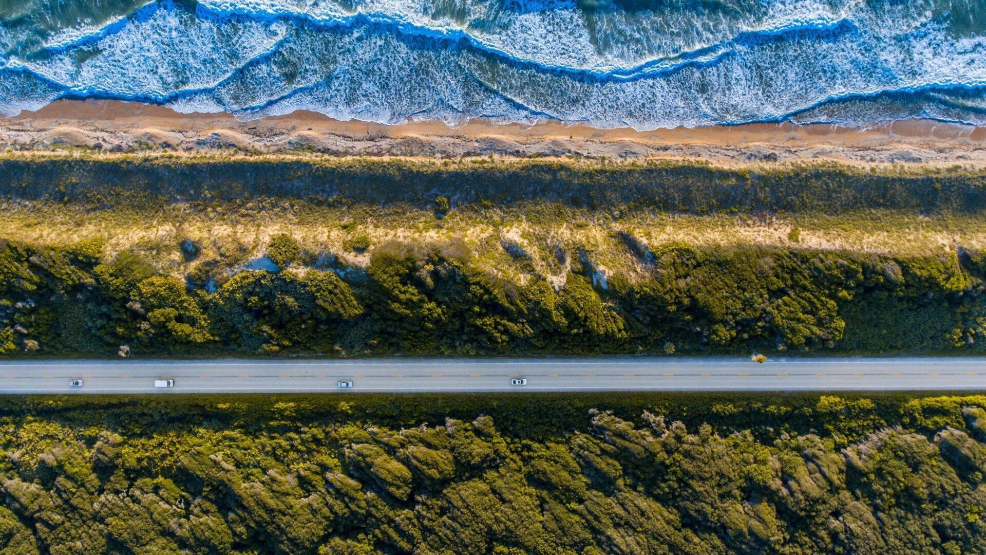 Vista aérea de una carretera costera que atraviesa un bosque exuberante con playa y olas del océano Índico
