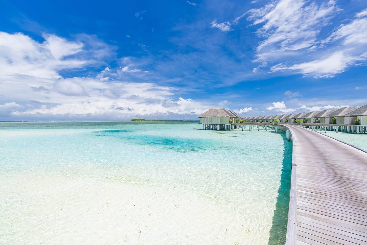 Vista aerea di un resort tropicale con bungalow sull’acqua, laguna turchese cristallina e cielo blu