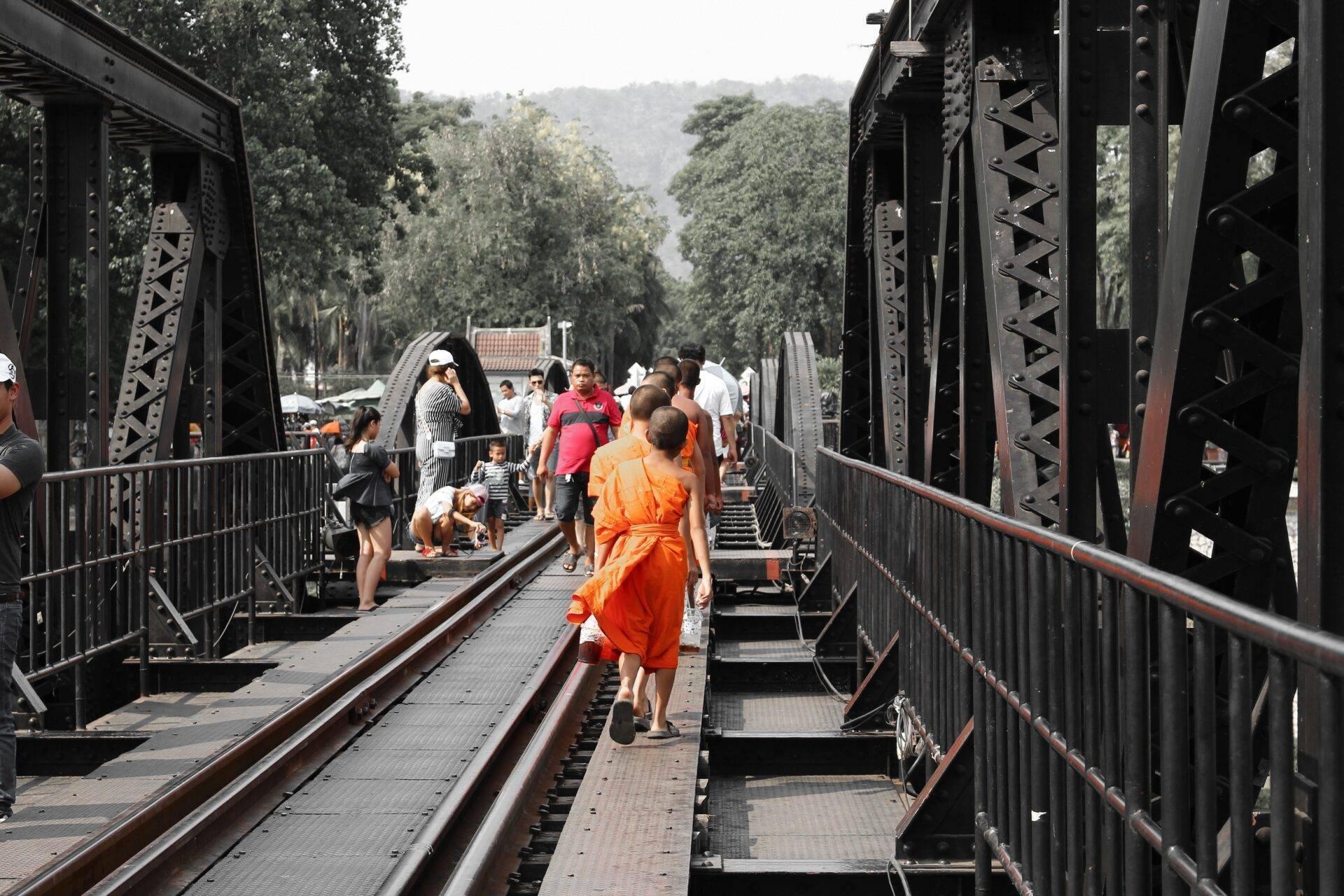Turistas cruzando un puente ferroviario de acero entre montañas boscosas en Tailandia