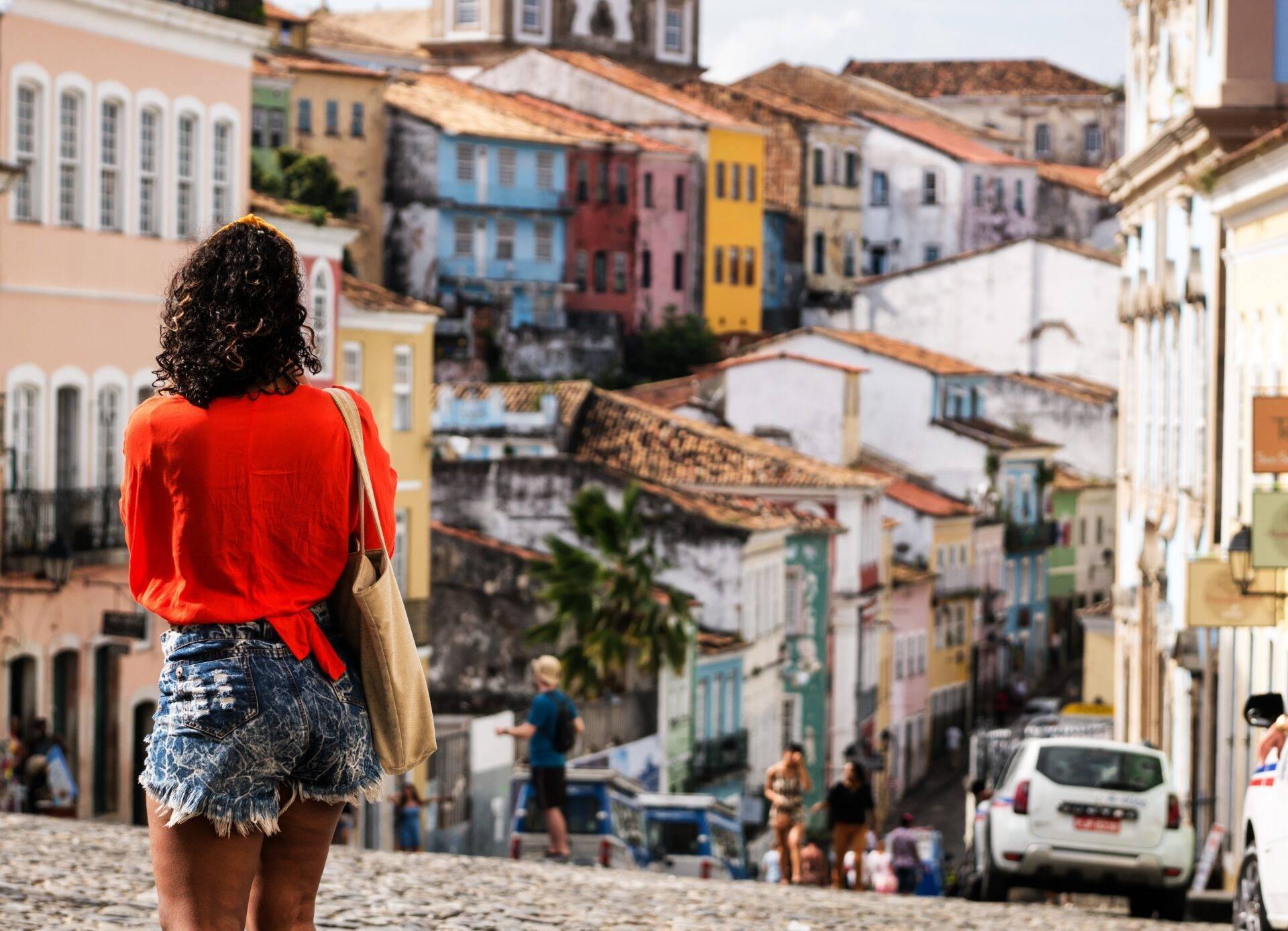 Una donna con la camicia rossa osserva una via acciottolata colorata con case coloniali tradizionali