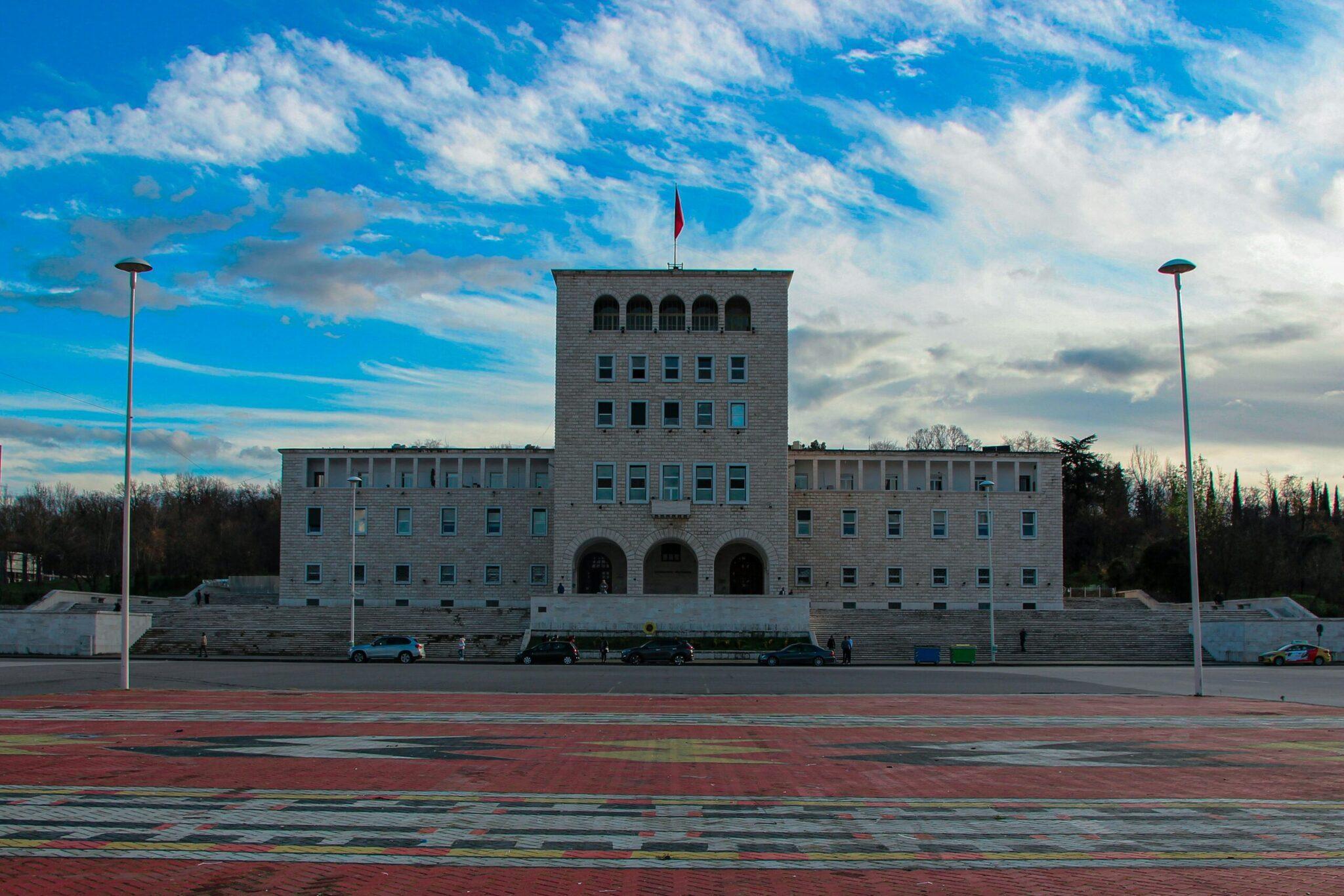 Ein modernes weißes Regierungsgebäude mit Nationalflagge, das einen weitläufigen gepflasterten Platz unter blauem Himmel überragt