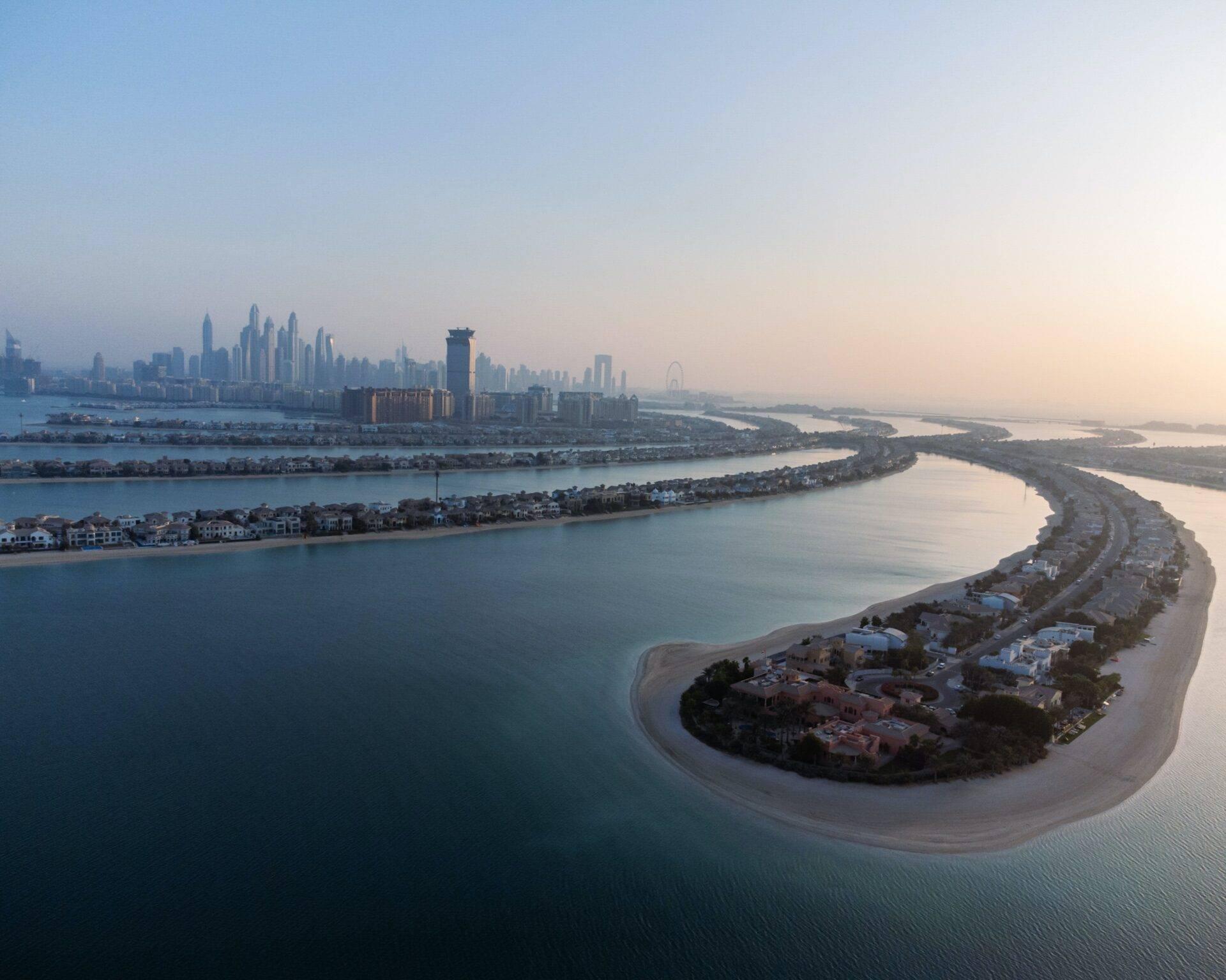 Luftaufnahme einer halbmondförmigen Kunstinsel mit Luxuswohnhäusern vor der Skyline einer Küstenmetropole