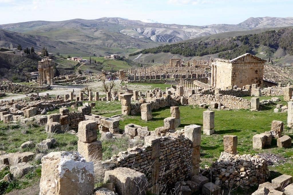 Ruinas antiguas con columnas de piedra dispersas en un paisaje montañoso y ondulado de color verde