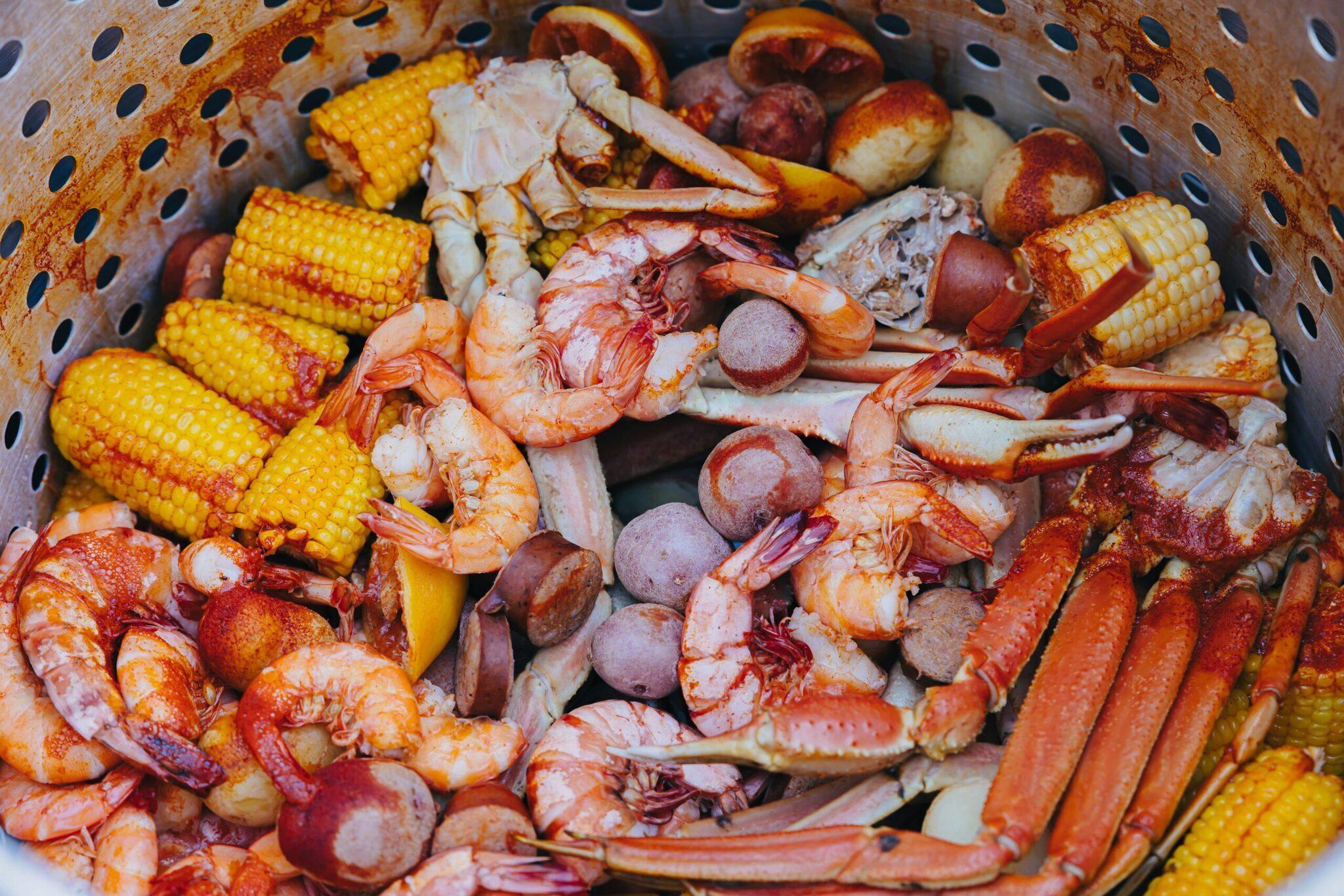 Un cestello forato colmo di frutti di mare cotti tra cui gamberetti, granchio, salsicce e mais grigliato
