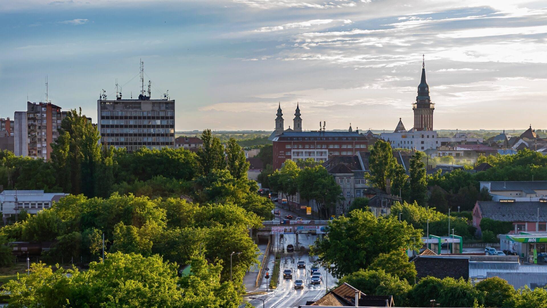 Panoramaansicht einer europäischen Stadt mit Kathedrale, modernen Gebäuden und üppiger Vegetation unter klarem Himmel
