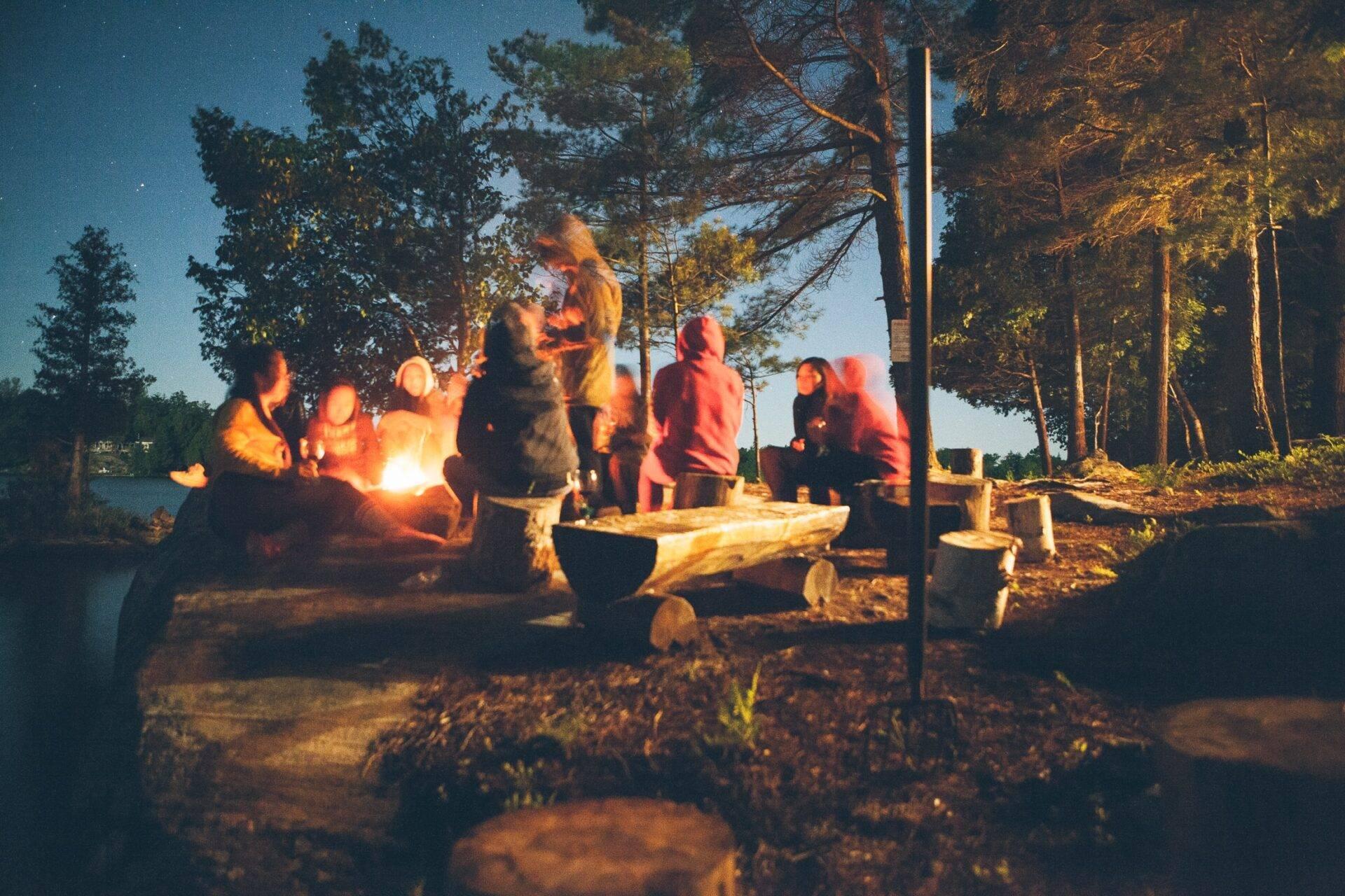 Eine Gruppe Menschen versammelt sich um ein Lagerfeuer im Wald bei einem winterlichen Abend