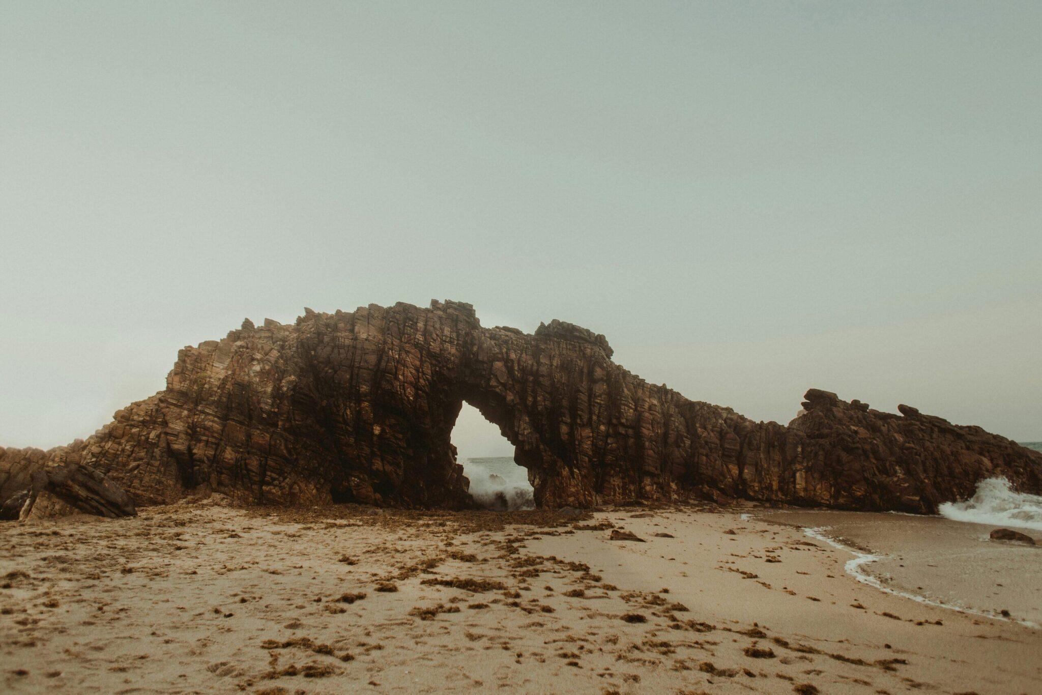 Un arco natural de roca erosionada en una playa desierta con el océano al fondo