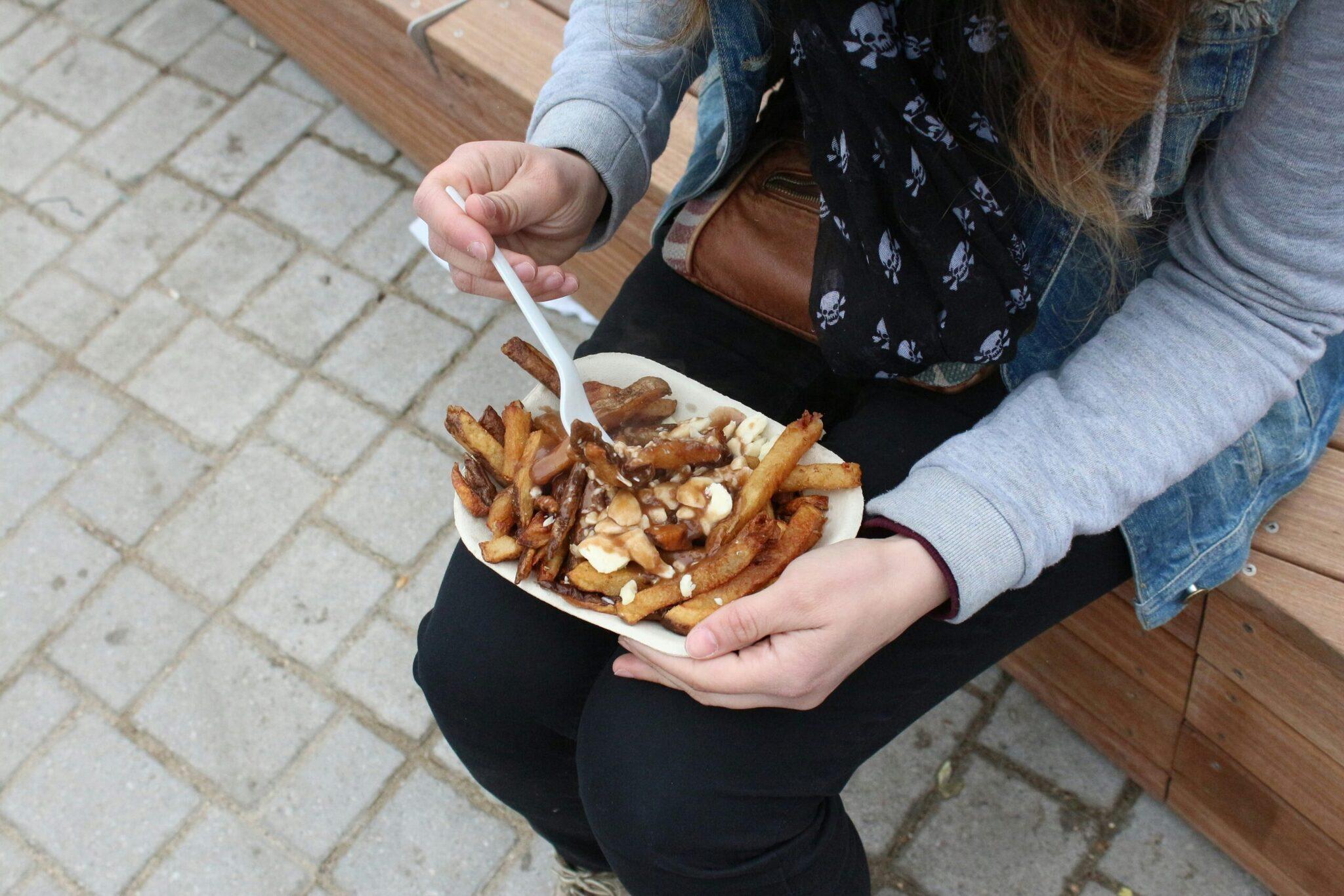Zwei Personen genießen auf einer gepflasterten Straße in Montréal Pommes frites mit Käse