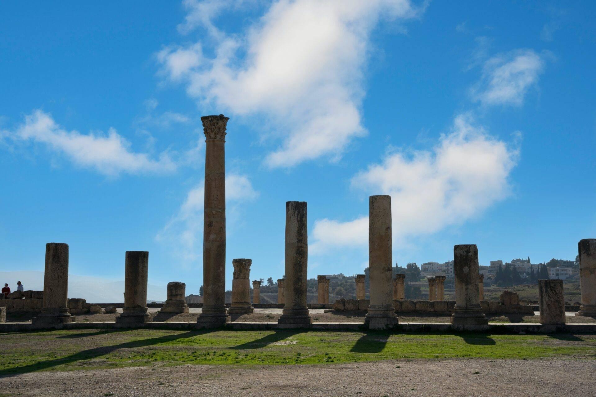 Ruinas antiguas con columnas de piedra en pie sobre un terreno herboso bajo un cielo azul con nubes