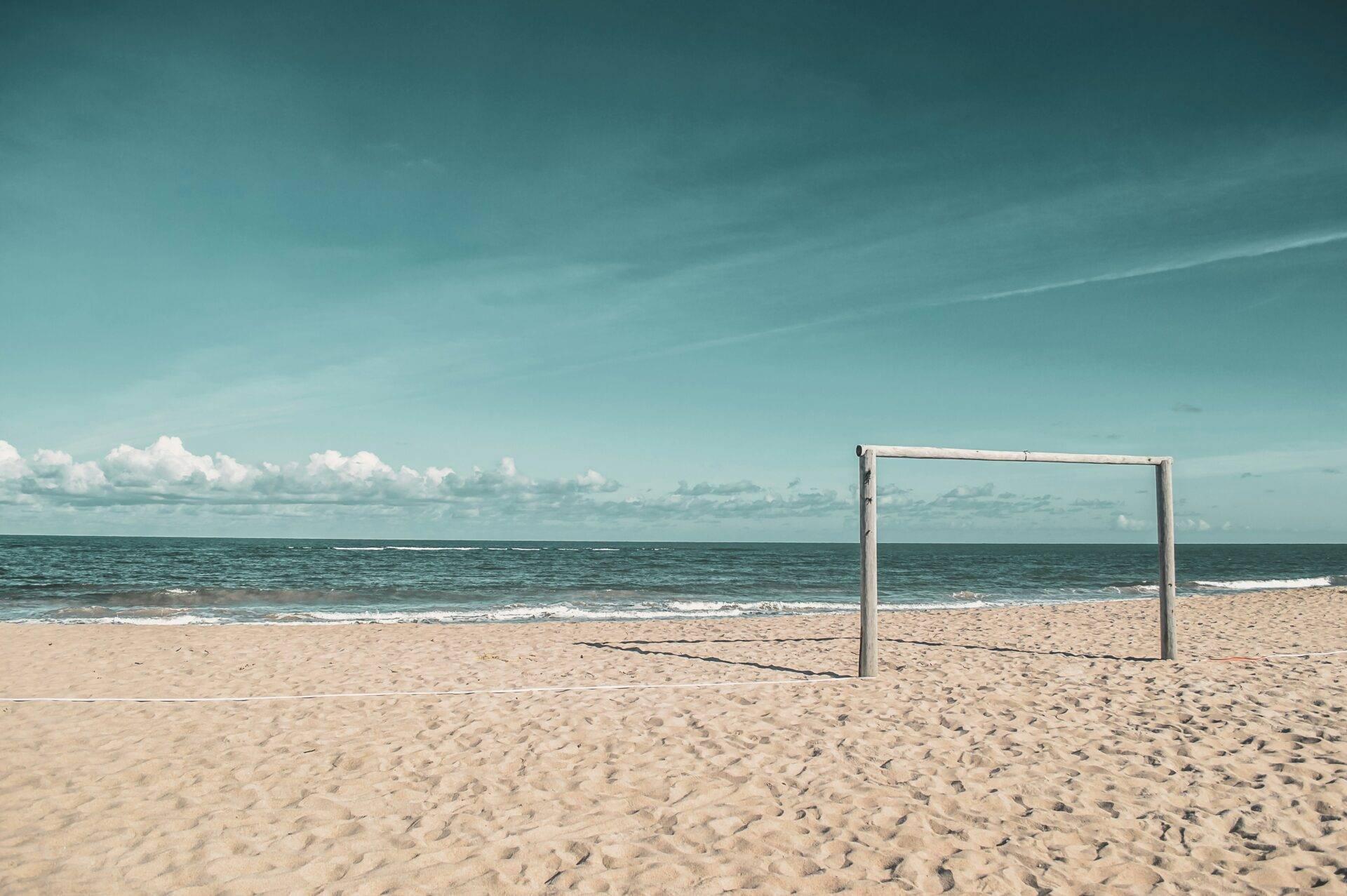 An empty beach volleyball frame on fine sand facing the turquoise ocean under a clear sky