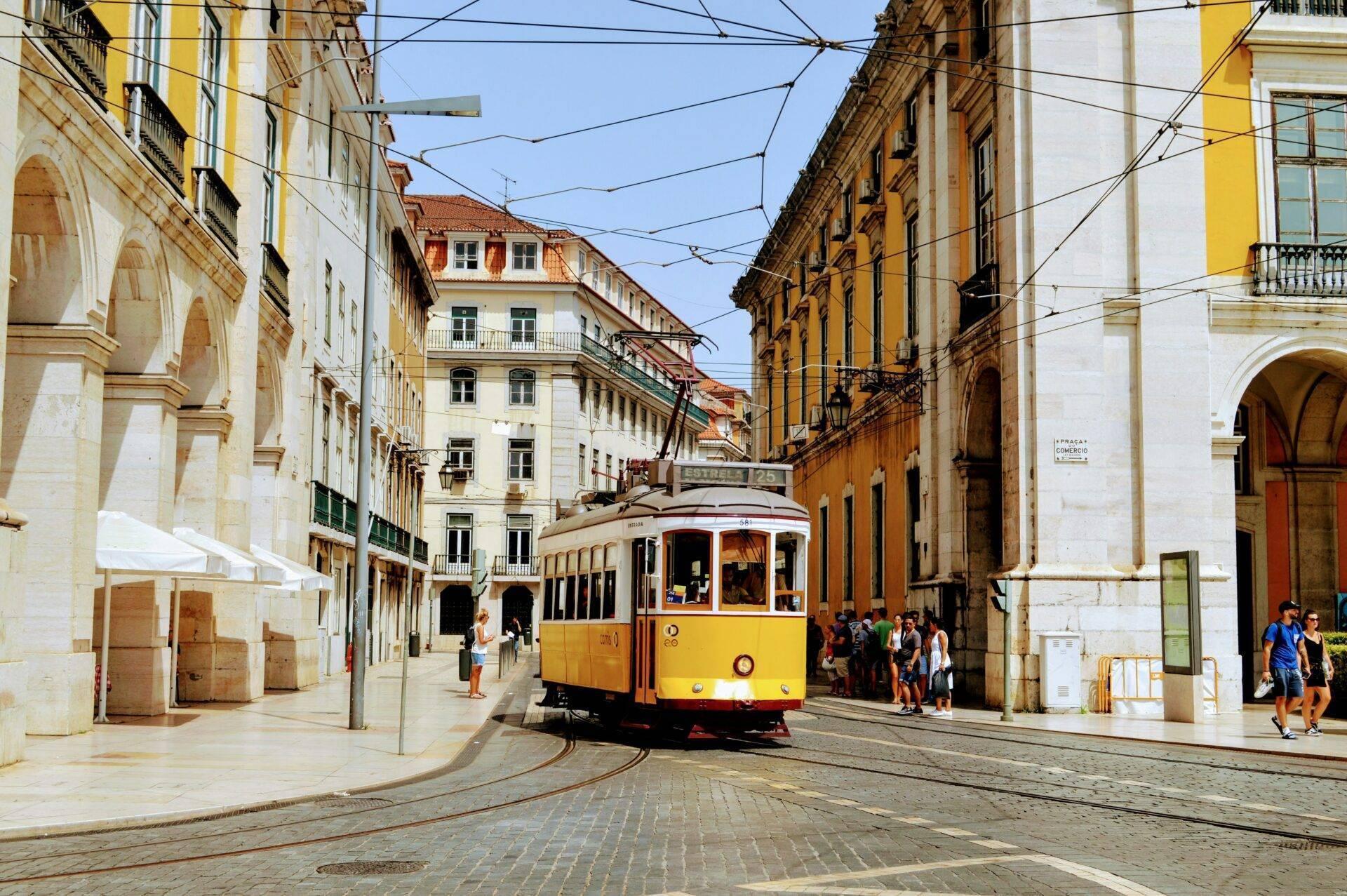 Un tram giallo e rosso percorre una via acciottolata di una città storica europea fiancheggiata da eleganti palazzi antichi