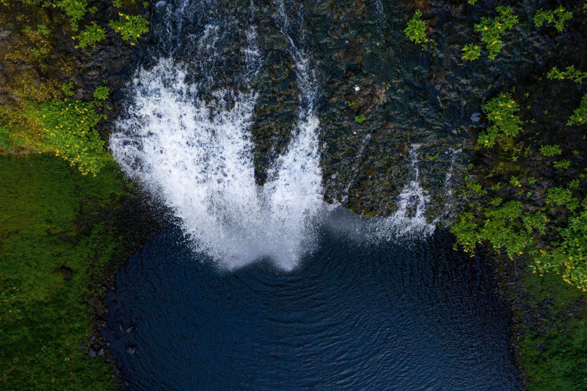 Vista aérea de una cascada torrencial que cae en una poza rocosa rodeada de exuberante vegetación verde