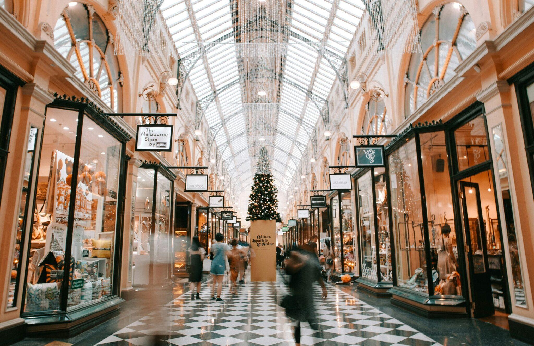 Galería comercial cubierta adornada con decoración navideña, árbol iluminado en el centro y tiendas elegantes